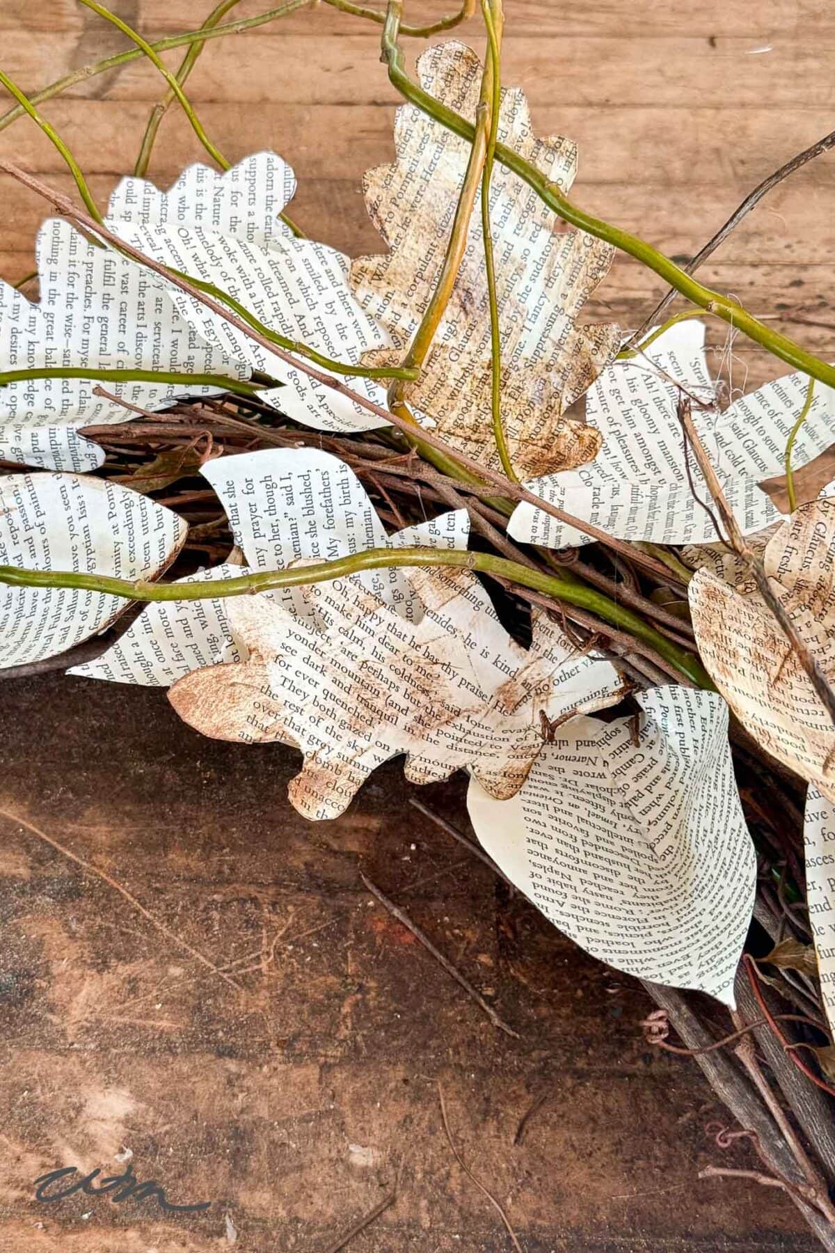 A bundle of artificial leaves made from book pages and attached to twigs, with a rustic wooden surface in the background.