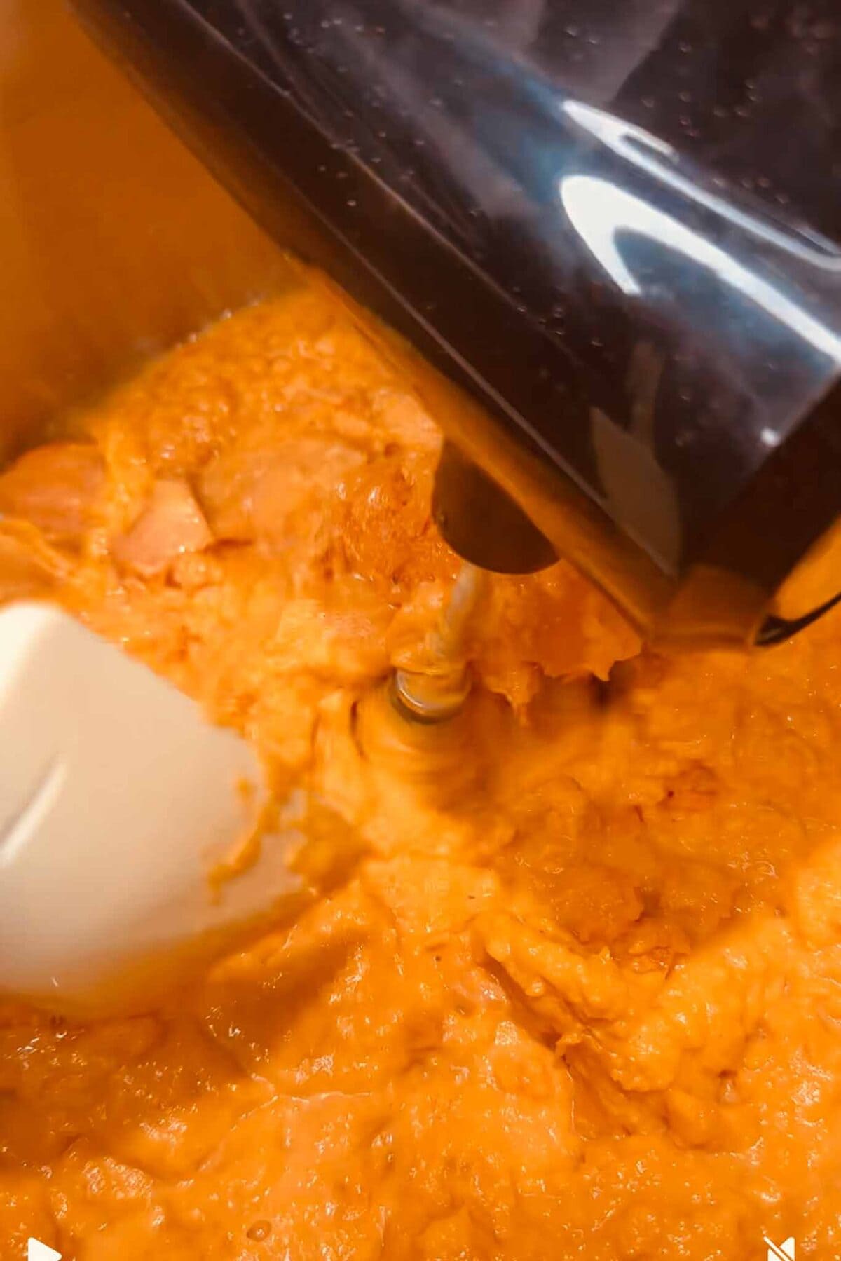 Close-up of a sweet potato mixture being blended in a food processor, with a plastic blade stirring the contents. The smooth, creamy texture makes it perfect for Thanksgiving or filling festive orange cups.