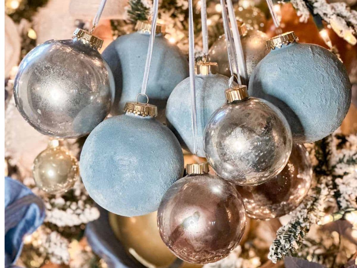 A close-up of a Christmas tree decorated with shiny blue and silver DIY velvet ornaments, surrounded by warm white lights and snow-dusted branches.
