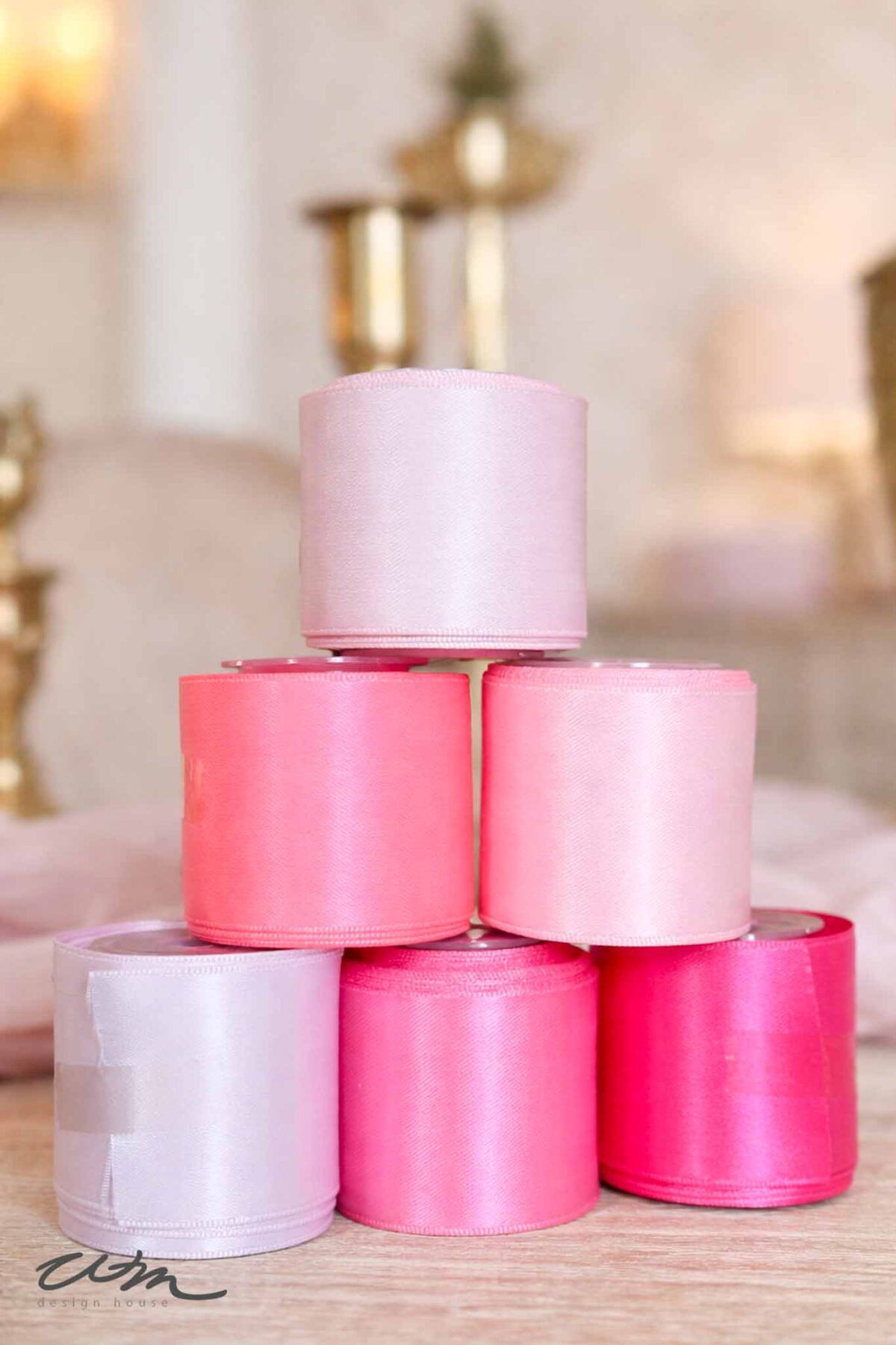 Six rolls of satin ribbon in shades of pink and lavender are stacked in a pyramid shape on a light surface, perfect for adding charm to any Valentine’s party for grandkids, with a softly blurred, elegant background.