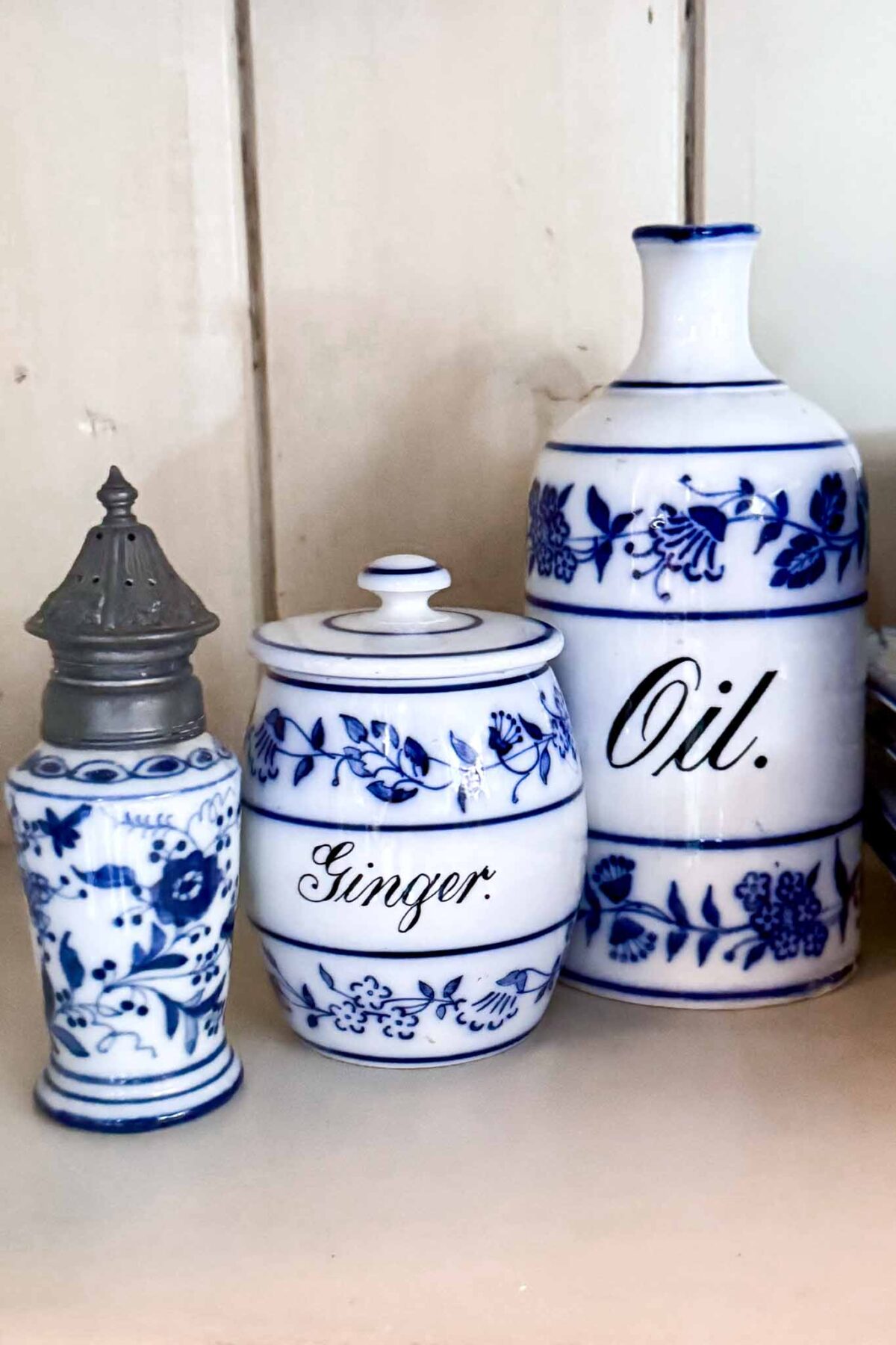 Three blue and white porcelain kitchen containers with floral designs are displayed; one labeled “Ginger,” a tall bottle labeled “Oil,” and a shaker with a metal lid, all arranged on a light shelf.