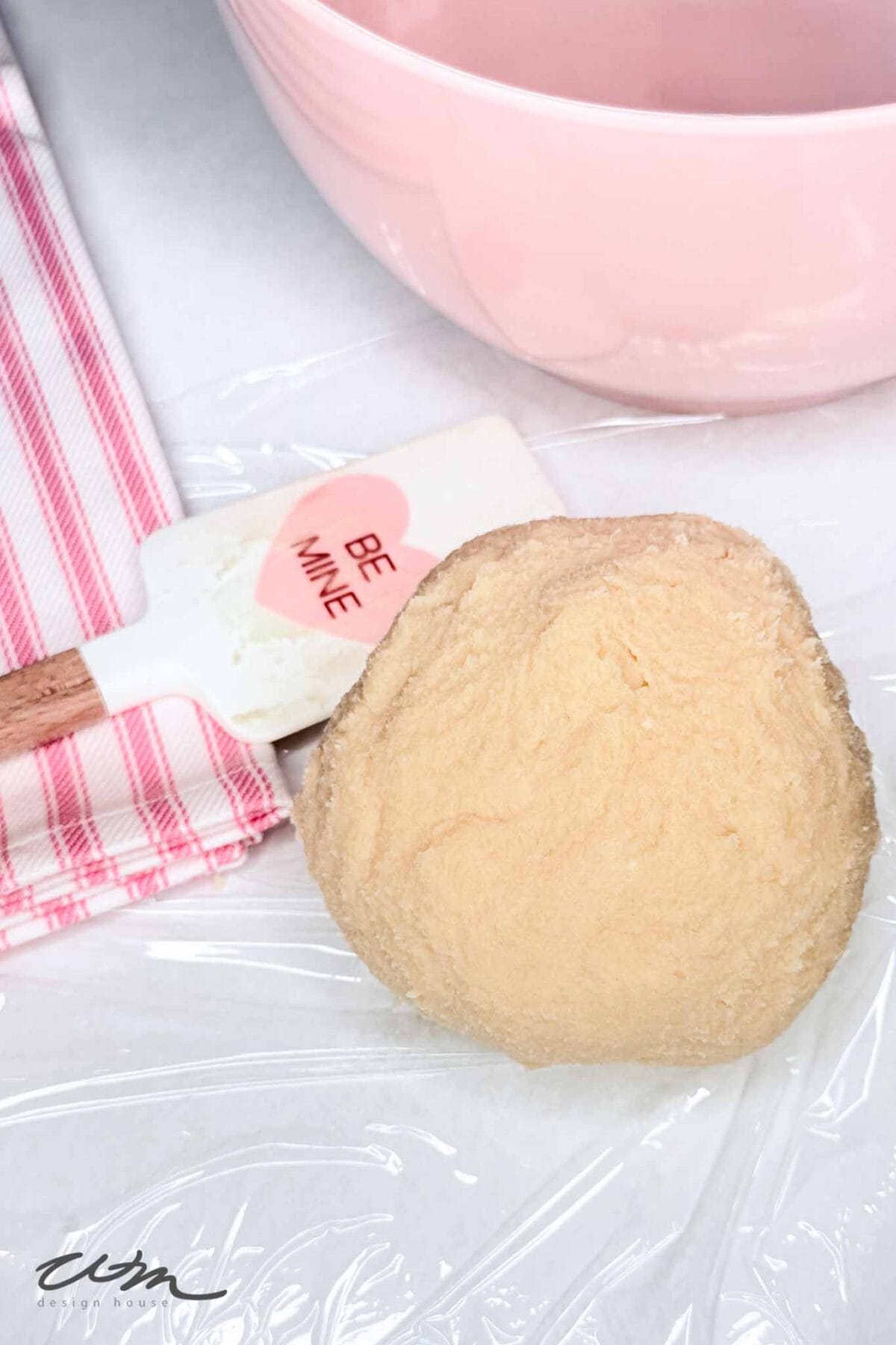 A ball of dough on plastic wrap next to a spatula.