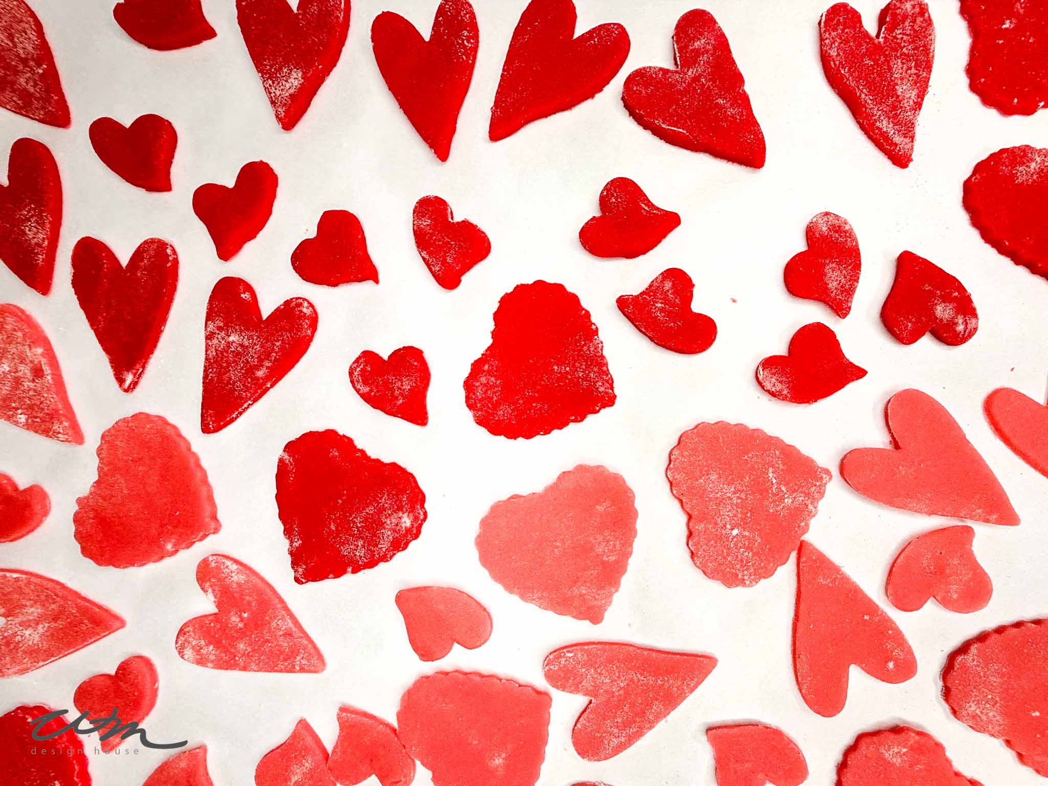 Various red and pink heart-shaped cookie cutters on a white background, some with scalloped edges and some smooth, arranged in a scattered pattern.