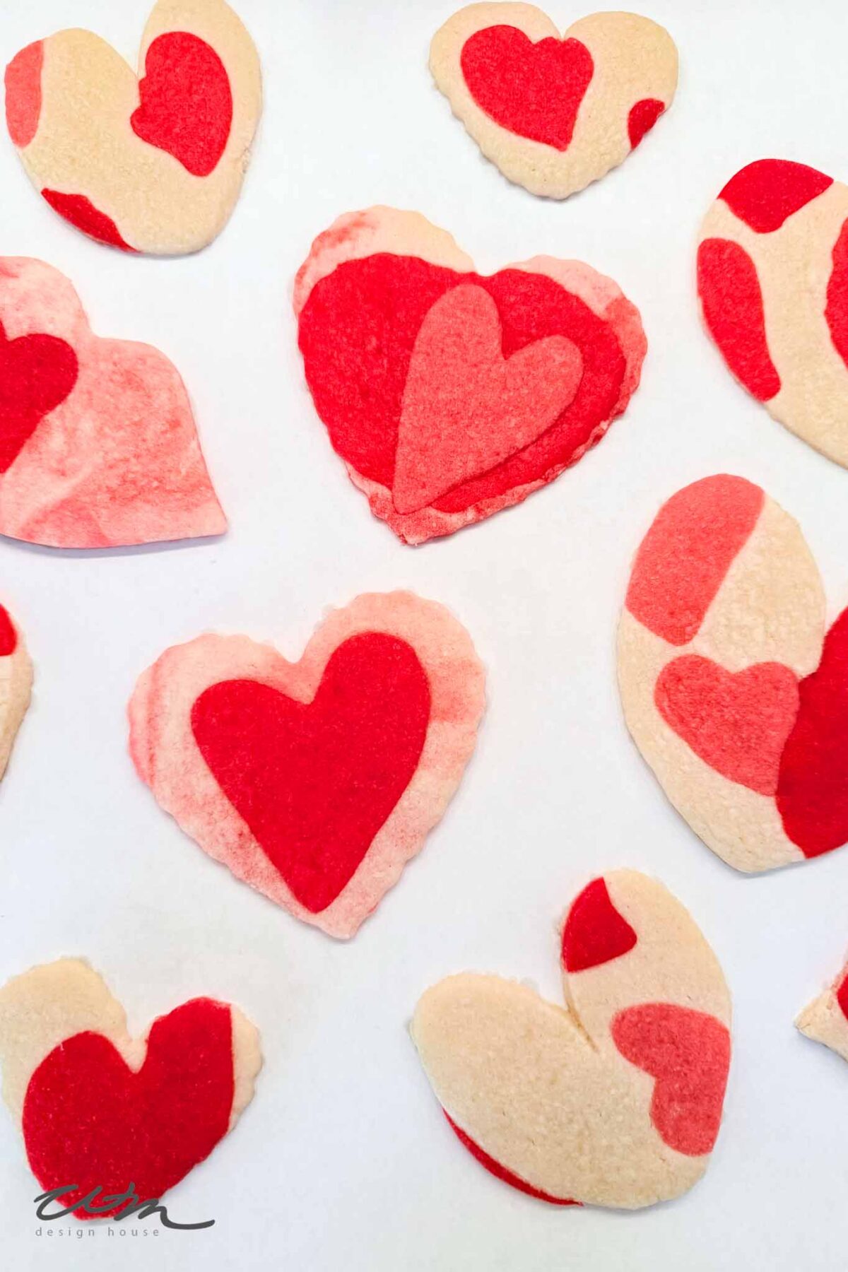 Heart-shaped sugar cookies with red and pink marbled and solid designs are arranged on a white surface, creating a festive and playful Valentine's Day theme.