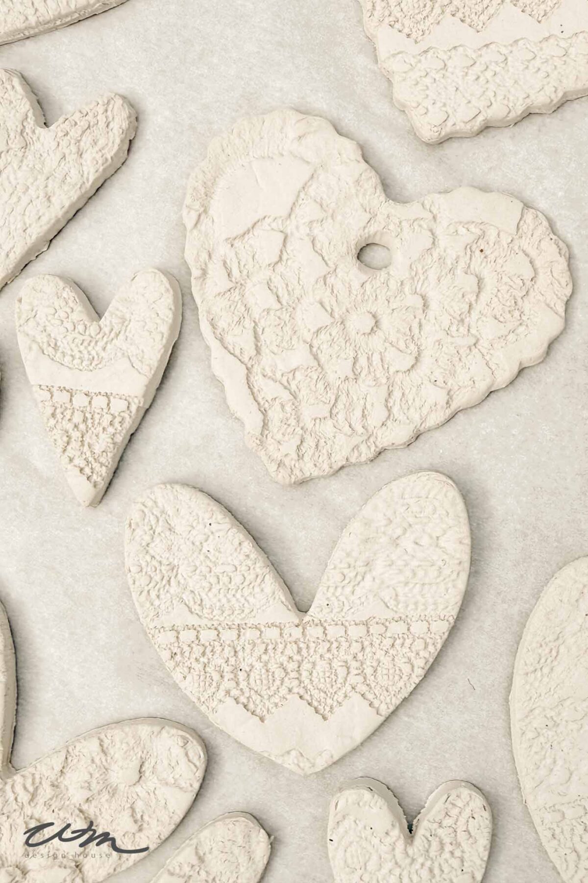 Several white, heart-shaped ornaments made from textured clay are arranged on a light surface. The clay hearts display lace-like patterns, giving them a delicate, handcrafted appearance.