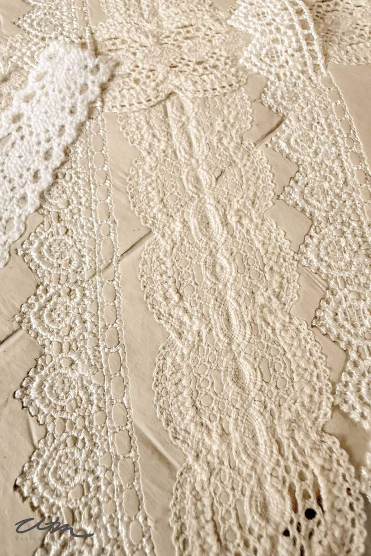 A close-up of various cream-colored lace ribbons arranged on a light surface, showcasing intricate patterns and delicate textures.
