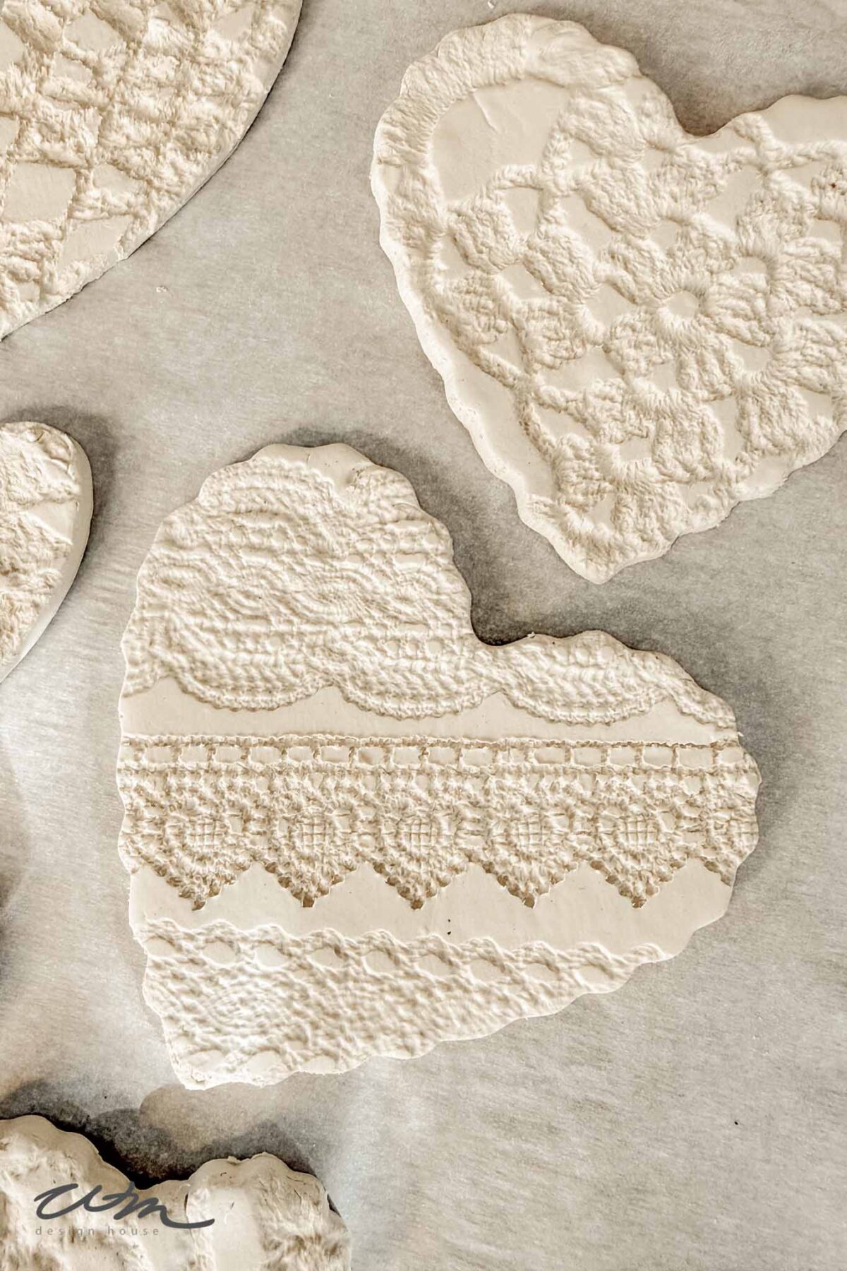 Heart-shaped clay ornaments with delicate, textured lace patterns pressed into the surface, displayed on a light background.