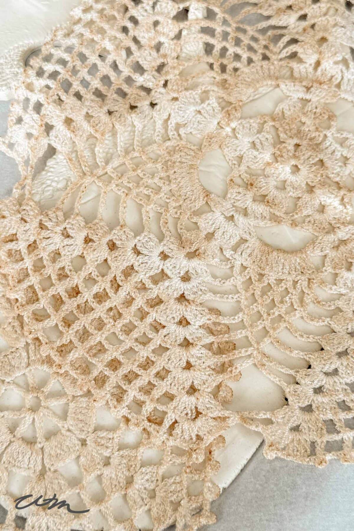 Close-up of a beige, intricately crocheted doily with floral and geometric patterns, placed on a white textured surface.