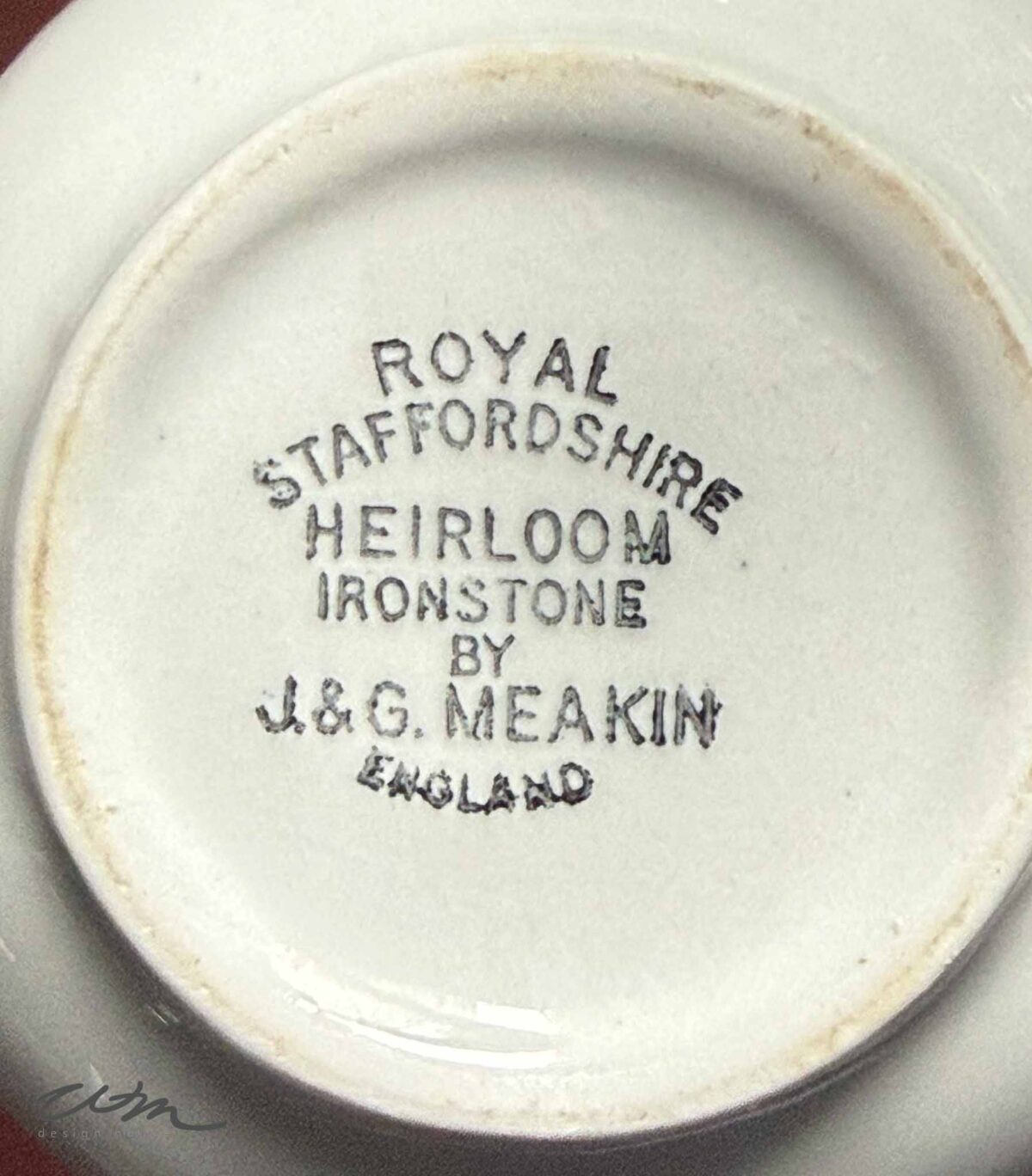 The bottom of a vintage white ironstone ceramic piece stamped with "Royal Staffordshire Heirloom Ironstone by J&G Meakin England" in black lettering.