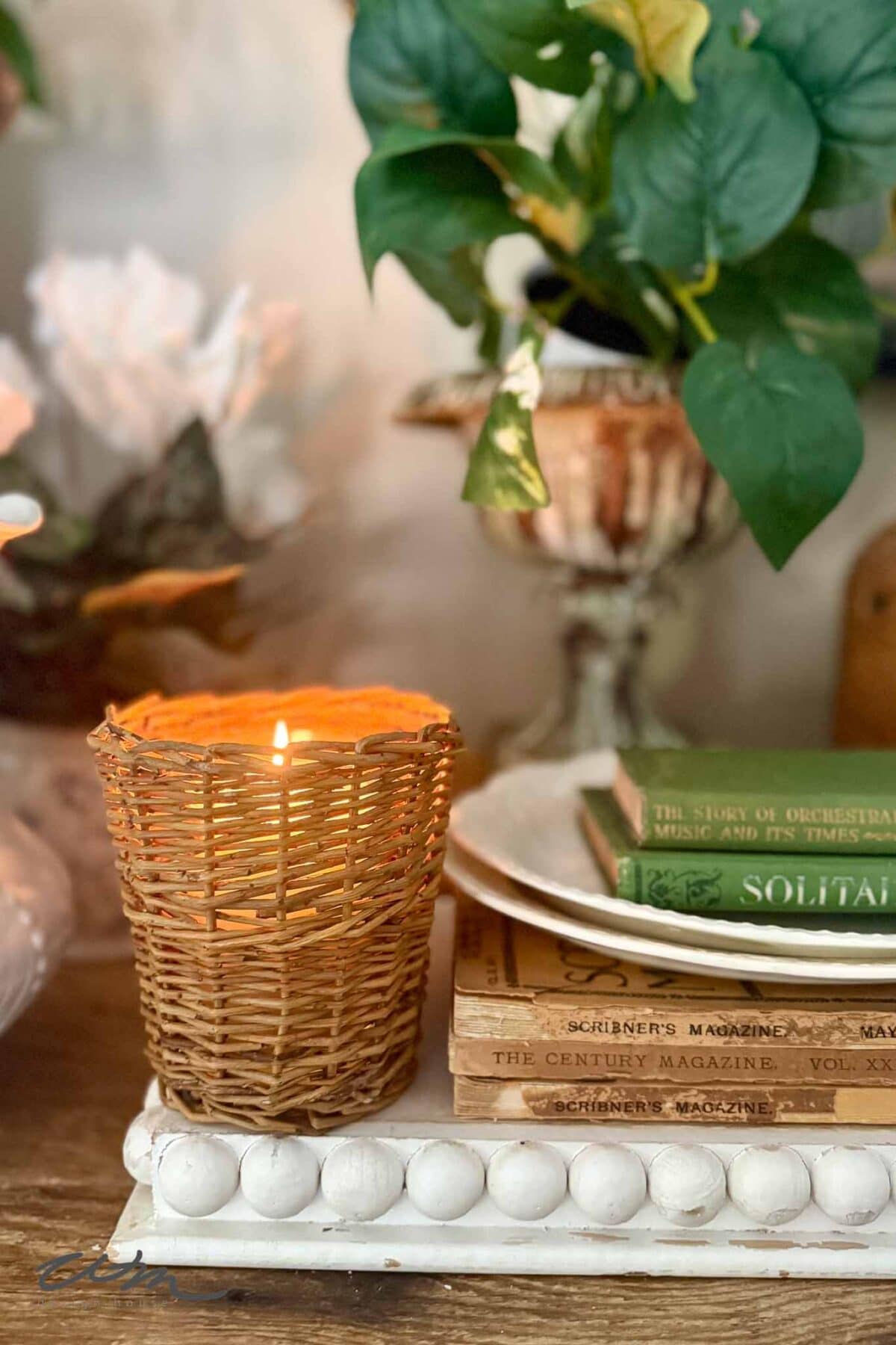 A candle in a wicker  basket next to a stack of books adds vintage charm to your Spring entry table decor.