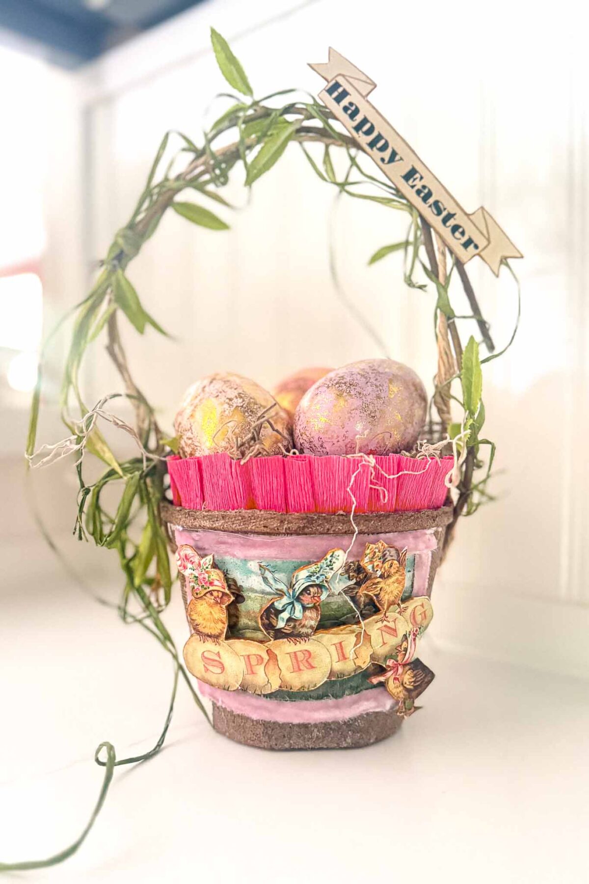 A decorative Easter basket made from a flower pot with a "SPRING" label, filled with painted eggs and adorned with vines, leaves, and a "Happy Easter" banner—perfect for simple Easter ideas or charming Spring Easter decor.