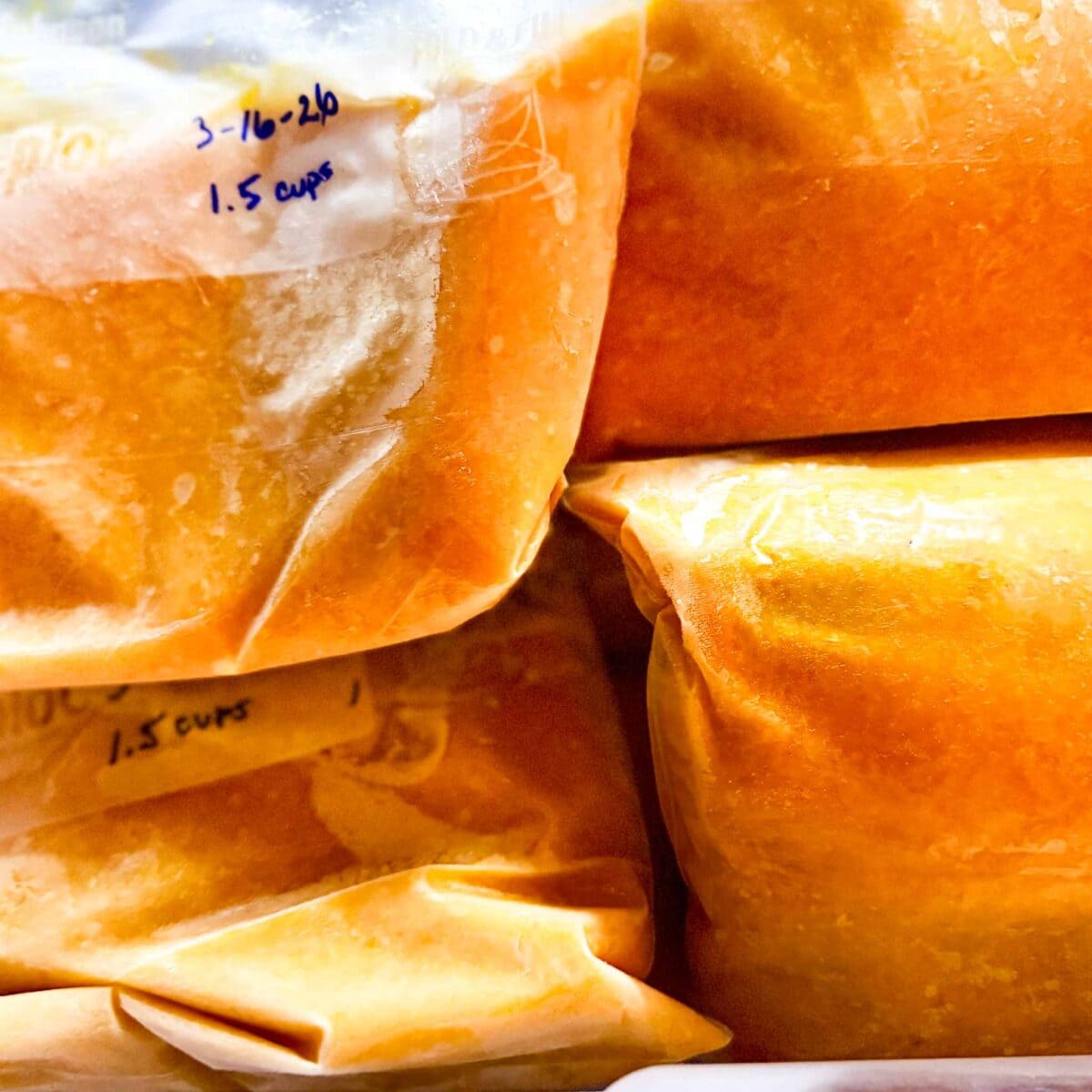 freezing tangerine puree in bags-Close-up of several labeled freezer bags filled with  tangerine puree, stacked together. One label reads "3-16-20, 1.5 cups" written in blue ink on the plastic.
