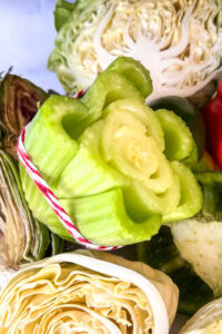 Close-up of assorted fresh vegetables, including a bundle of celery stalks tied with red and white string, surrounded by cabbage halves and other vegetables—perfect inspiration for vegetable block printing projects.