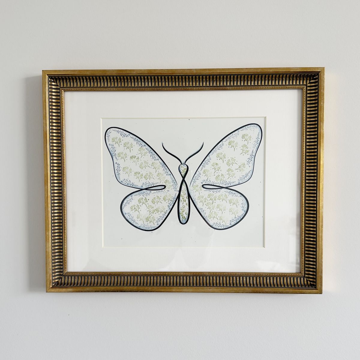 Framed artwork of a butterfly with wings filled with a delicate floral pattern, displayed against a white background and bordered by a gold frame.