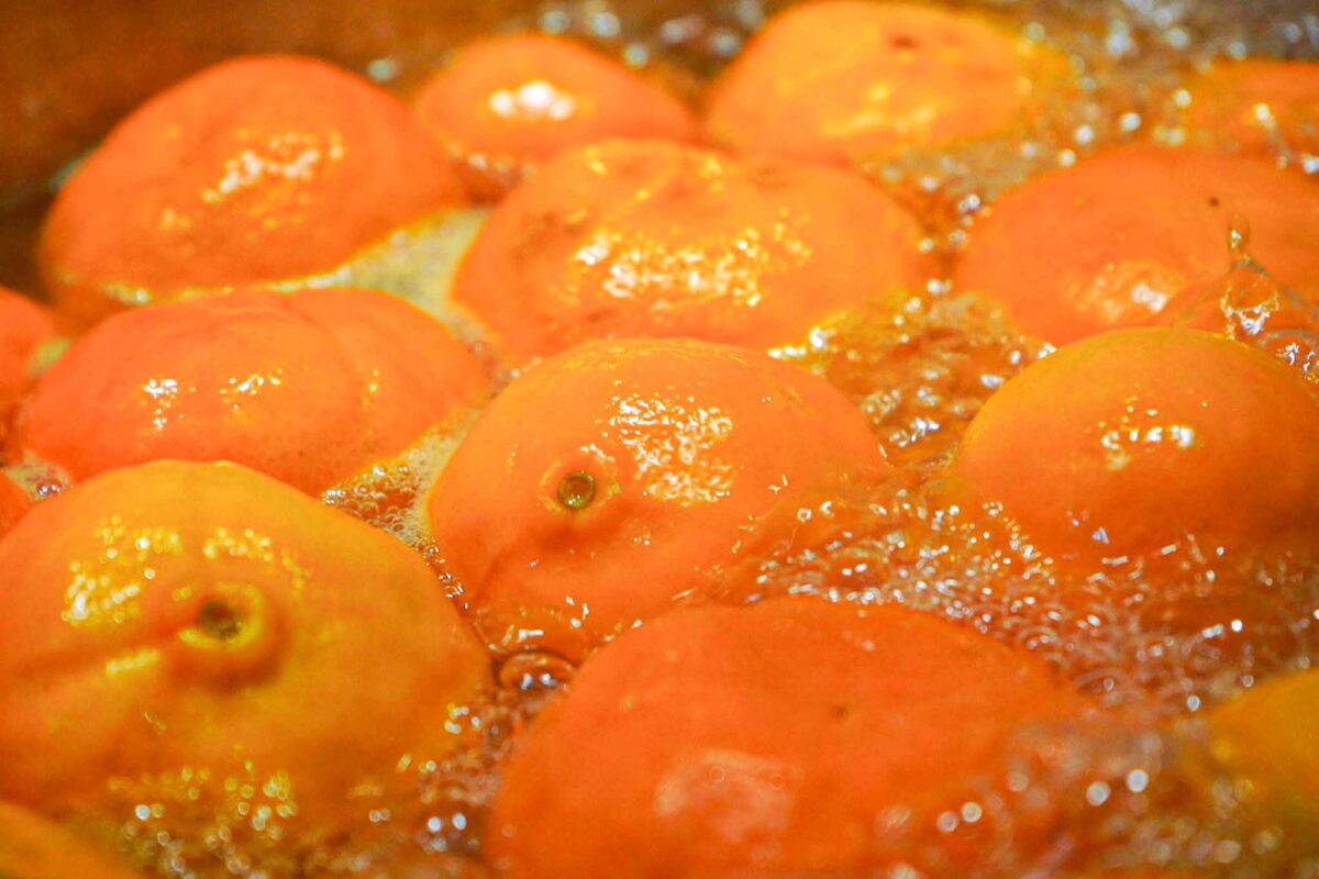 Whole oranges are being boiled in bubbling water, their bright orange peels glistening under the heat.