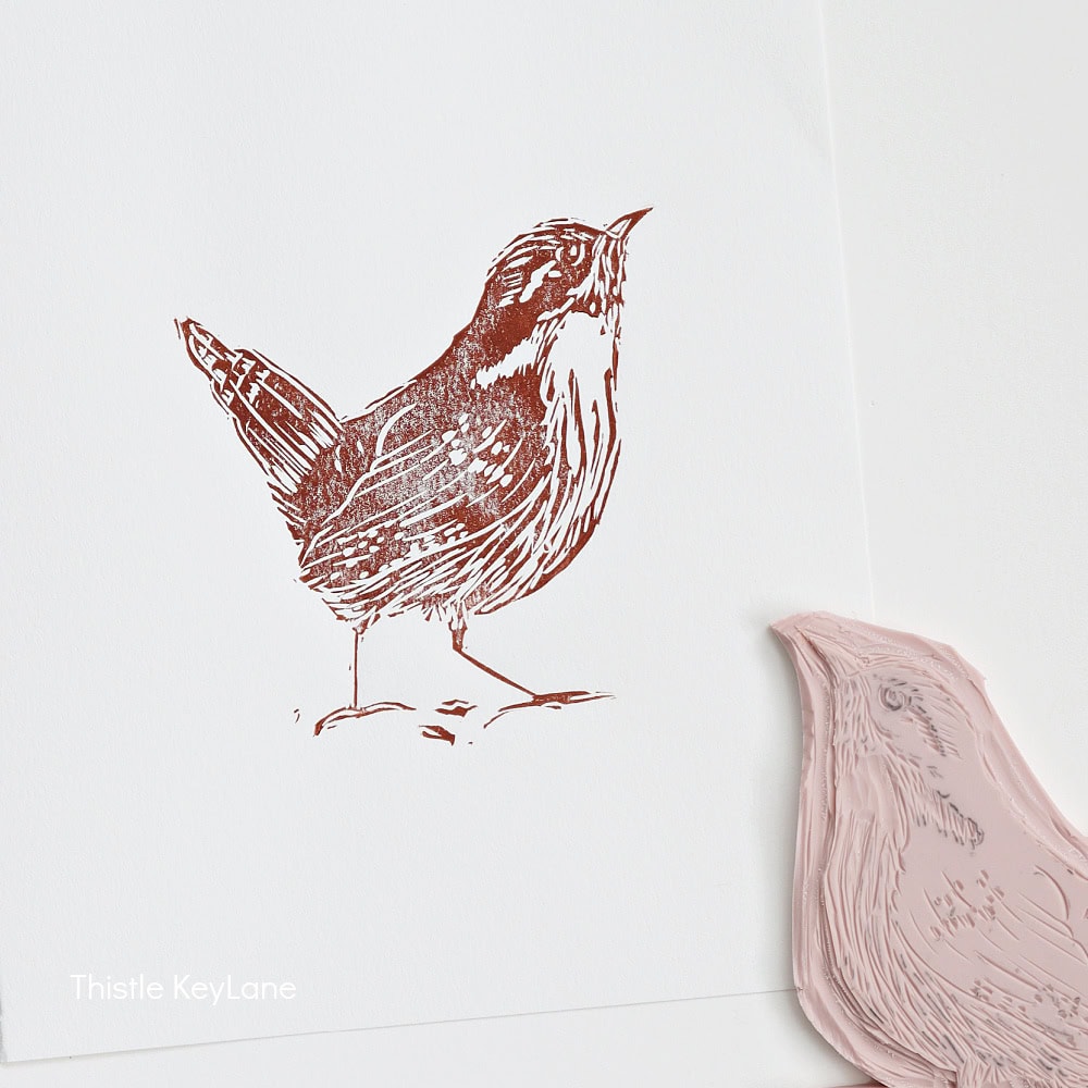 A hand-carved rubber stamp and its brown ink print of a bird standing on the ground, shown on white paper. The stamp is placed next to its printed image.