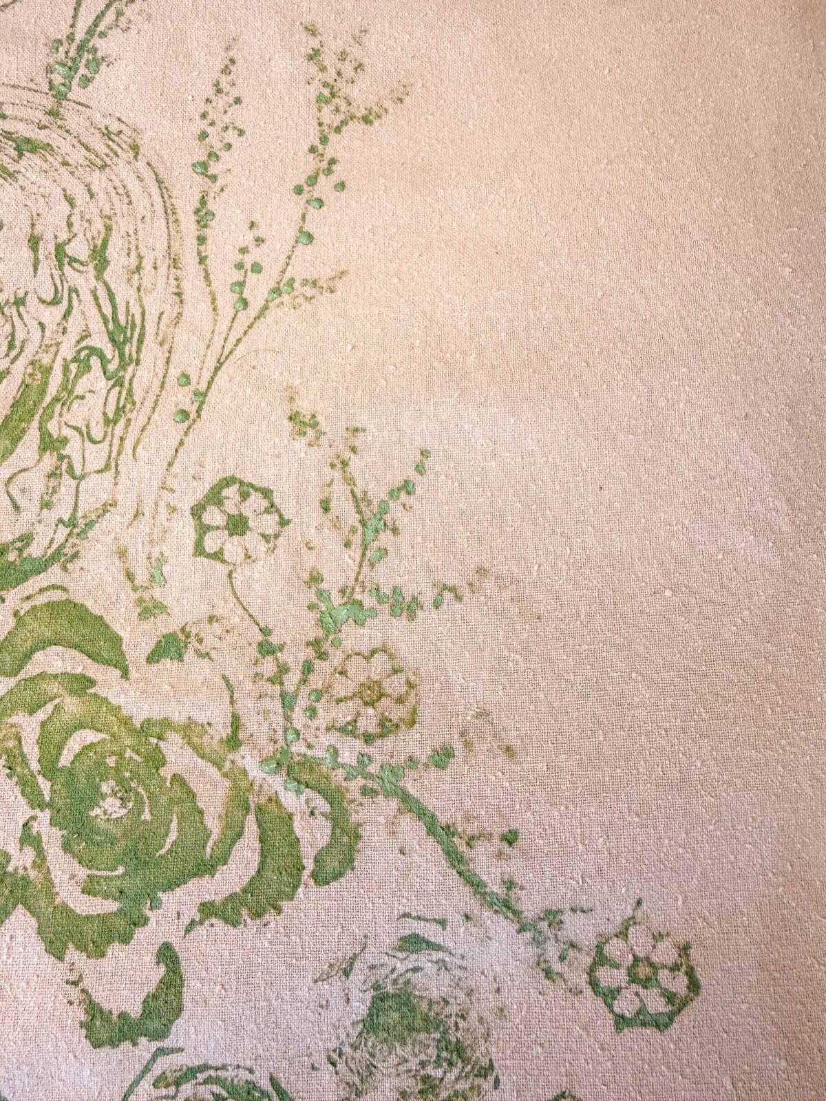 A close-up of a textured beige surface with a green floral pattern, featuring abstract flowers and leaves and subtle raised details.