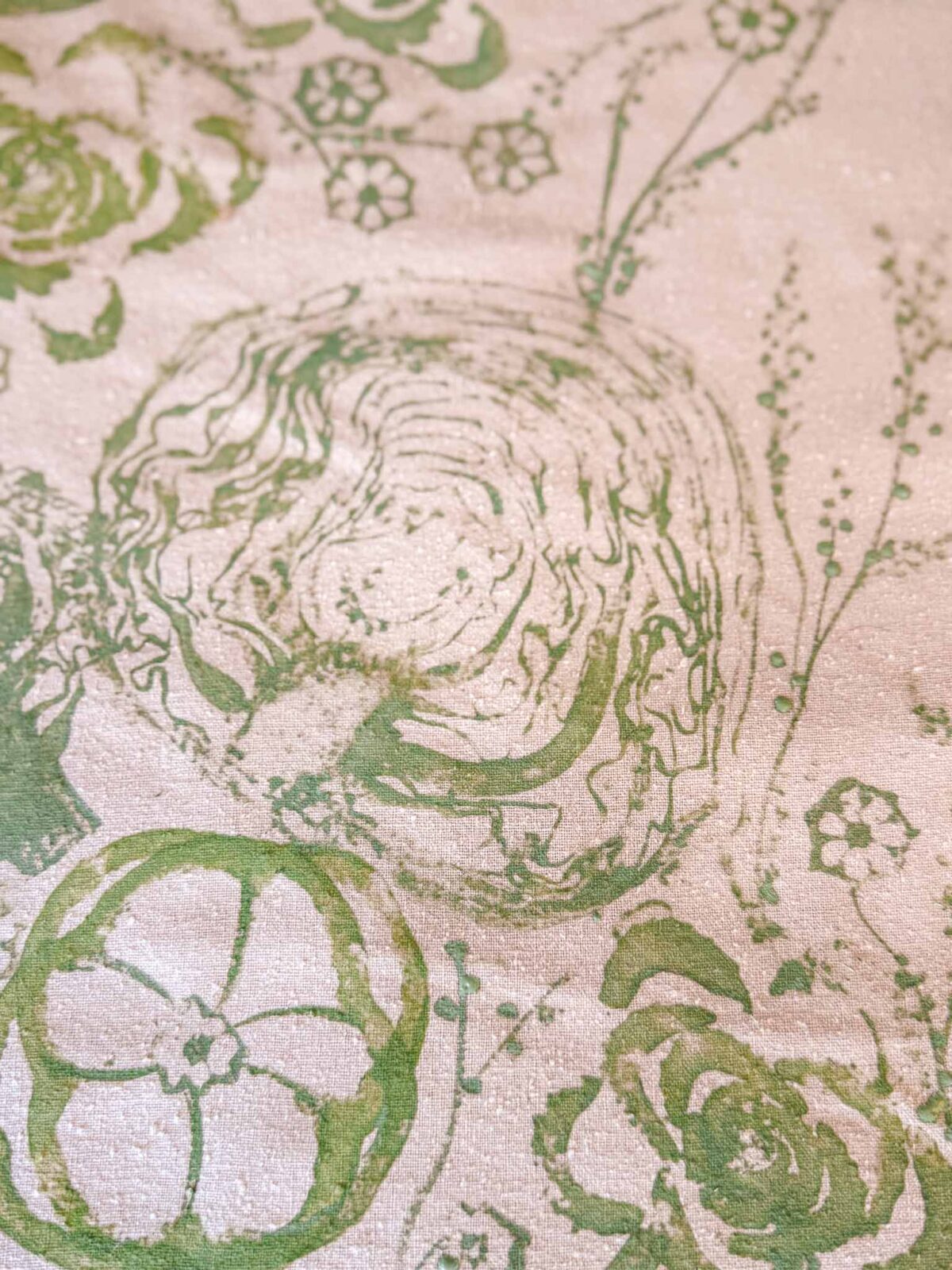 Green abstract floral and organic shapes are printed on a beige textured surface, with swirling patterns and circular flower-like forms scattered throughout the image.