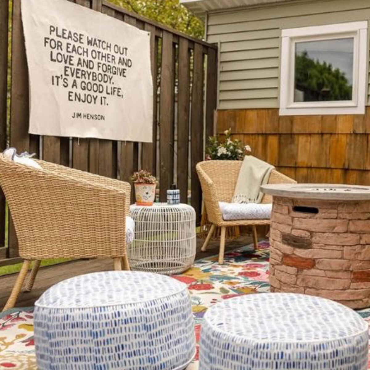 Cozy outdoor patio with wicker chairs, round poufs, a fire pit, and a colorful rug. Vintage Easter decorating ideas add charm, while a banner reads: "Please watch out for each other and love and forgive everybody…" – Jim Henson.