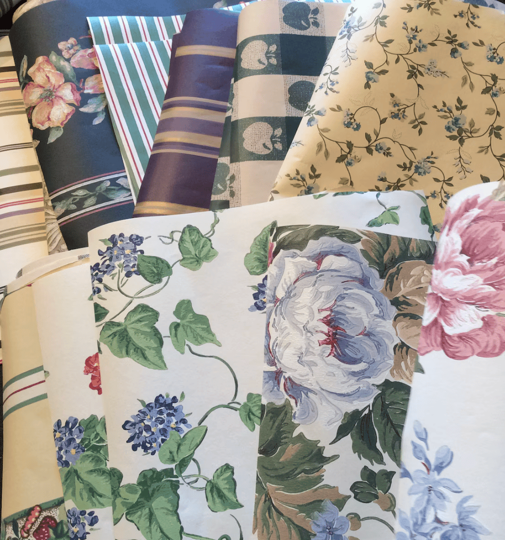 A variety of wallpaper samples with different floral and striped patterns in blues, greens, pinks, and creams are displayed overlapping each other—the best way to use leftover wallpaper is to line a lampshade for a creative touch.