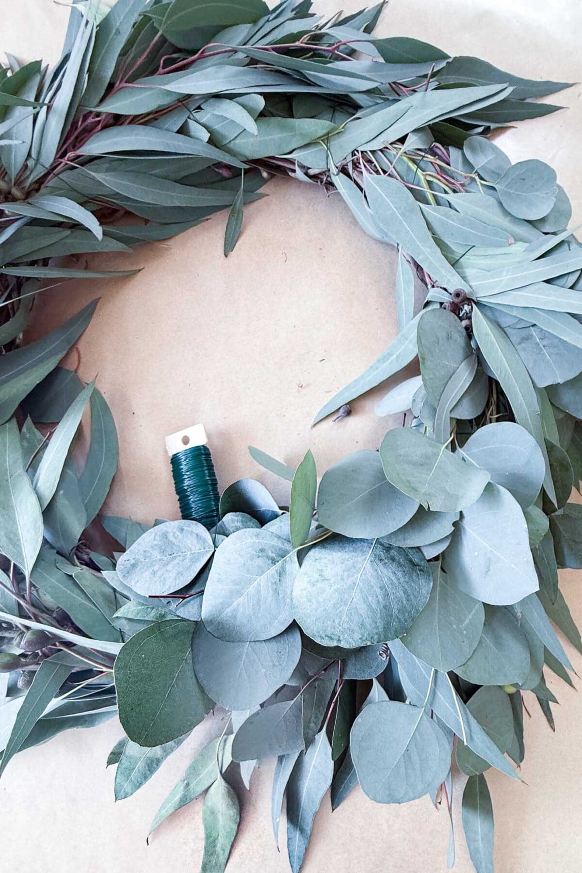 A partial eucalyptus wreath is being made with a spool of green floral wire in the center.