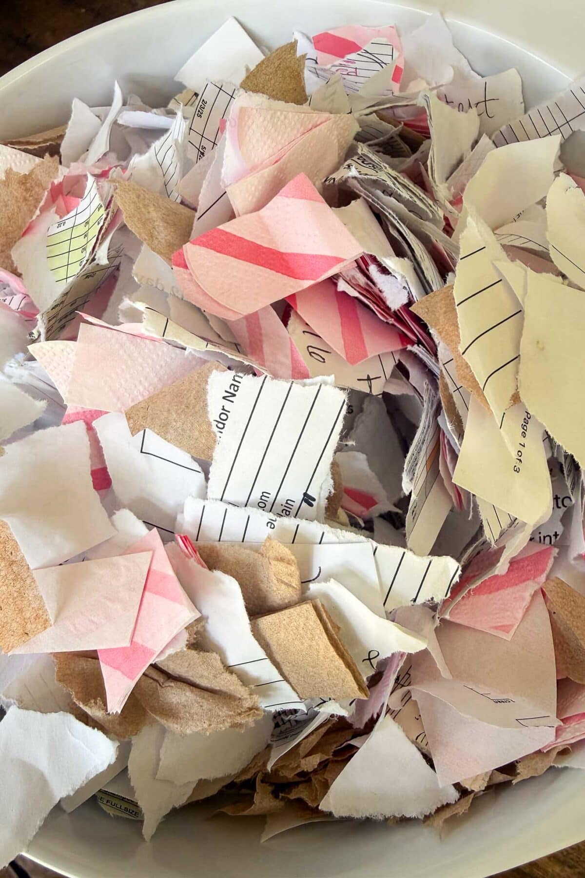 A white bowl filled with various torn pieces of paper, including lined, pink, white, and brown scraps—perfect for DIY Seed Paper or adding texture to handmade cards and other creative stationery projects.