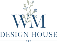 Logo for WM Design House featuring blue serif letters "WM" above "DESIGN HOUSE," with a sprig of greenery and delicate blue flowers artfully arranged behind the logo.