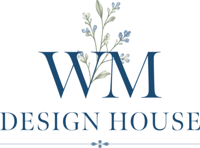 Logo with large blue letters "WM" featuring delicate blue flowers and green leaves, above the words "DESIGN HOUSE" in blue capital letters. The background is white with a small decorative line below.