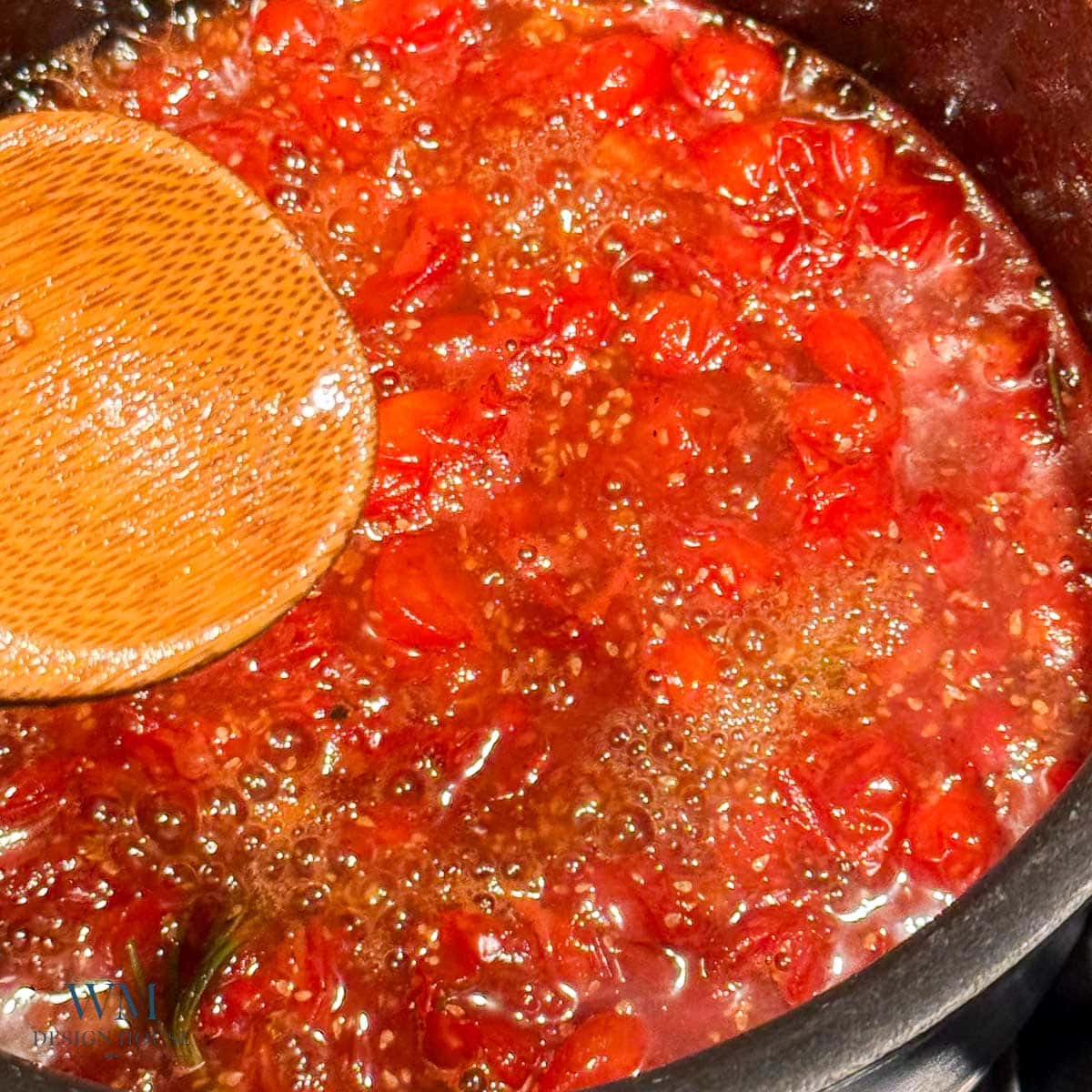A close-up of a bubbling tomato sauce with chopped tomatoes in a pot, being stirred with a wooden spoon.