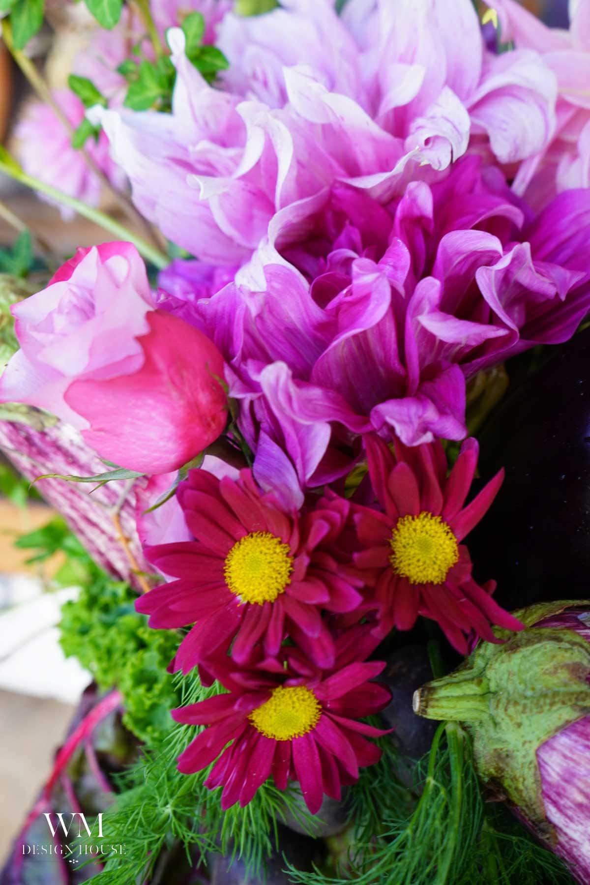A vibrant bouquet of pink and magenta flowers, including daisies and dahlias, is mixed with green foliage and an artichoke.