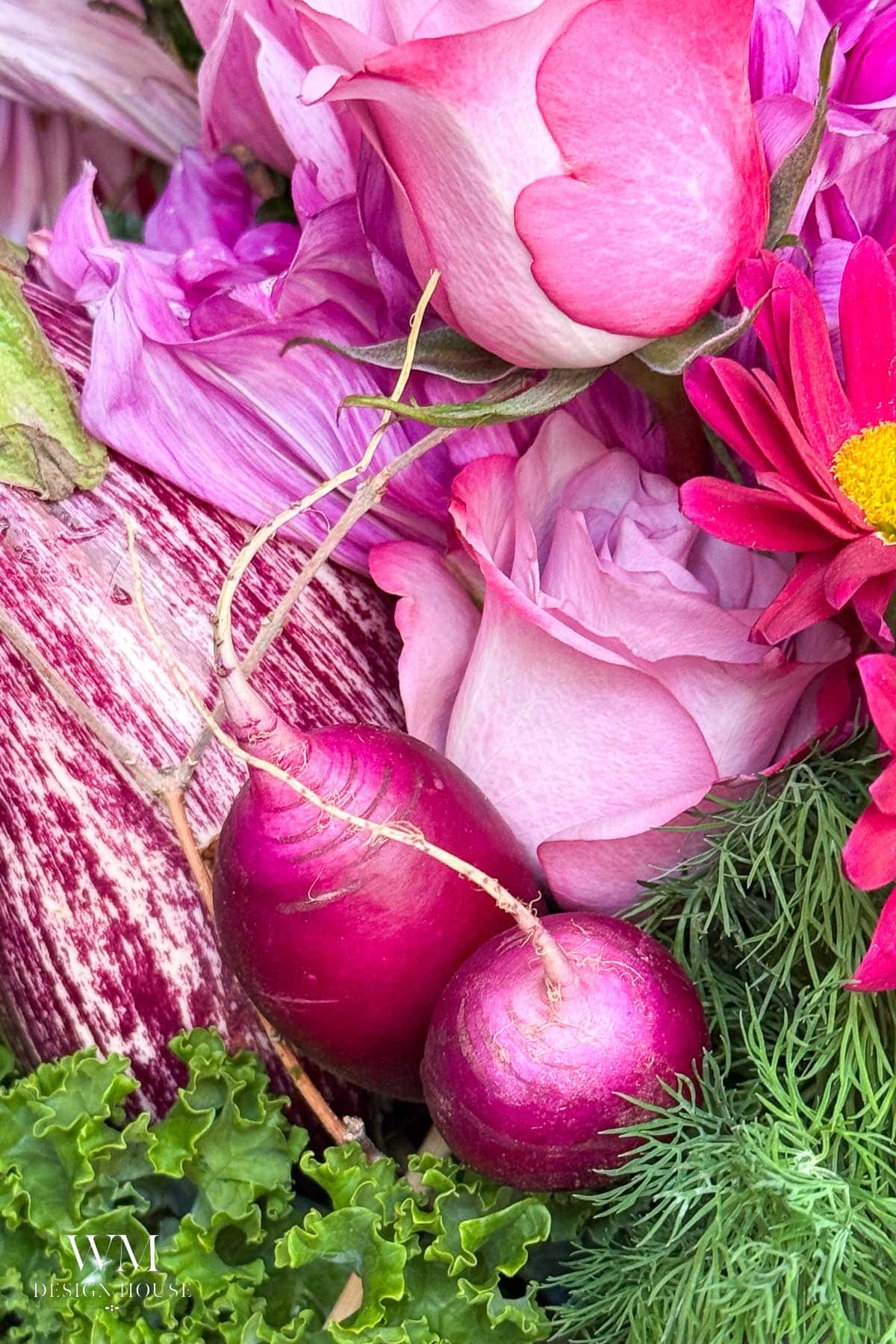 Two pink radishes nestled among pink roses, striped eggplant, and assorted greenery, including dill and kale, in a vibrant, colorful arrangement.