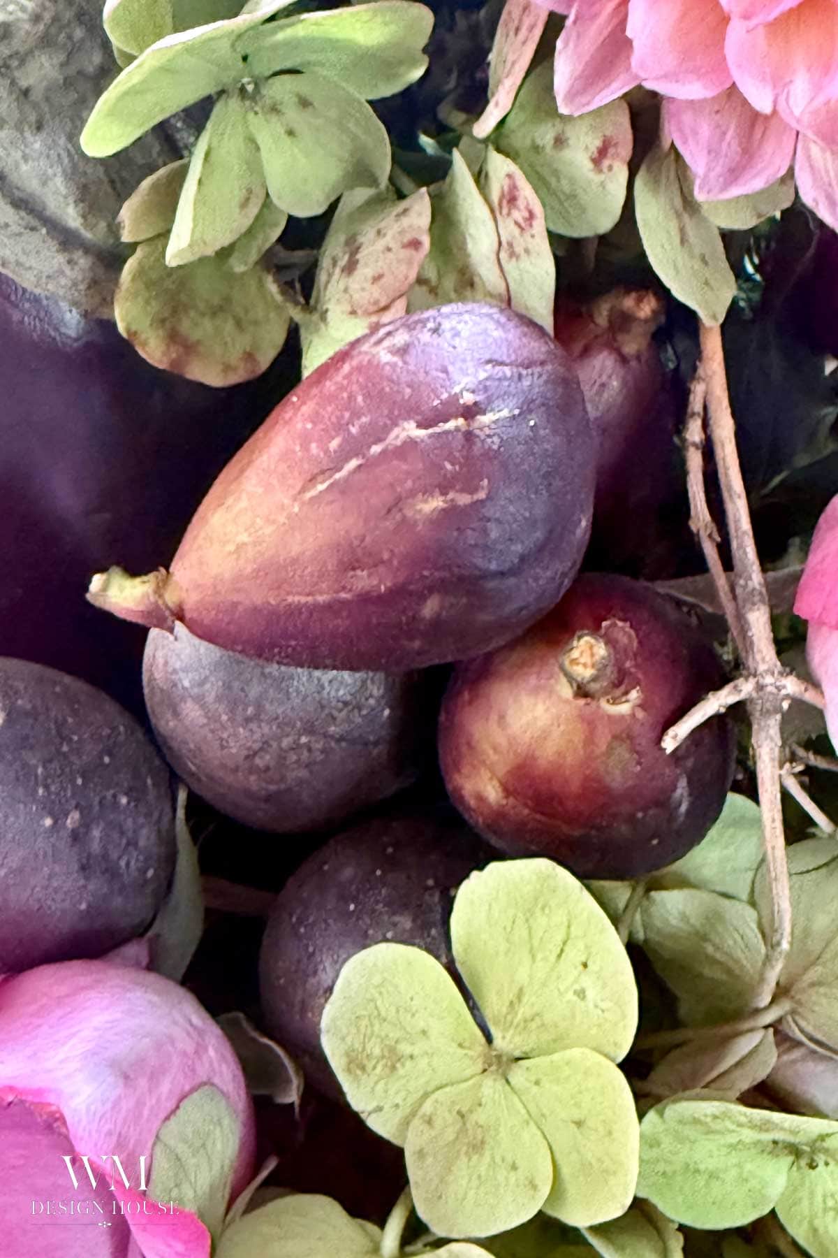 Assorted ripe figs clustered with green hydrangea petals and pink flowers create a vegetable-centerpiece, displaying a mix of textures and colors in a close-up natural arrangement.