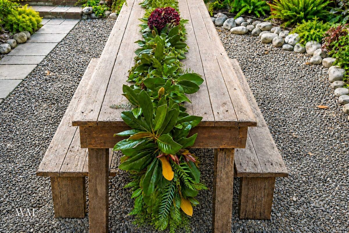 Magnolia and Eucalyptus Runner Before the Flowers laying on a farmhouse wooden table in a garden.