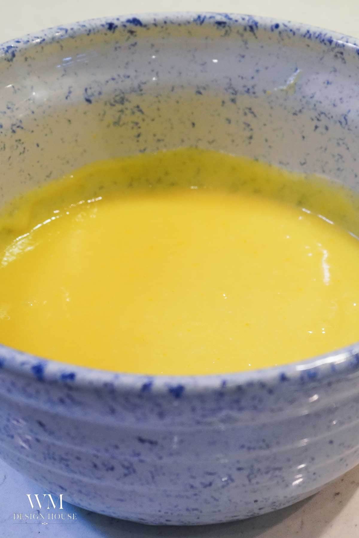 A blue-speckled ceramic bowl filled with a smooth, creamy Meyer Lemon Curd, its vibrant yellow hue standing out beautifully against the light surface.