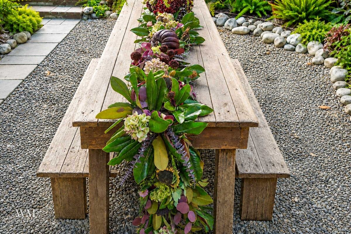Greenery table runner of magnolia and eucalyptus with dried dahlias, hydrangeas, and a plum pumpkin running down a nine foot outdoor table