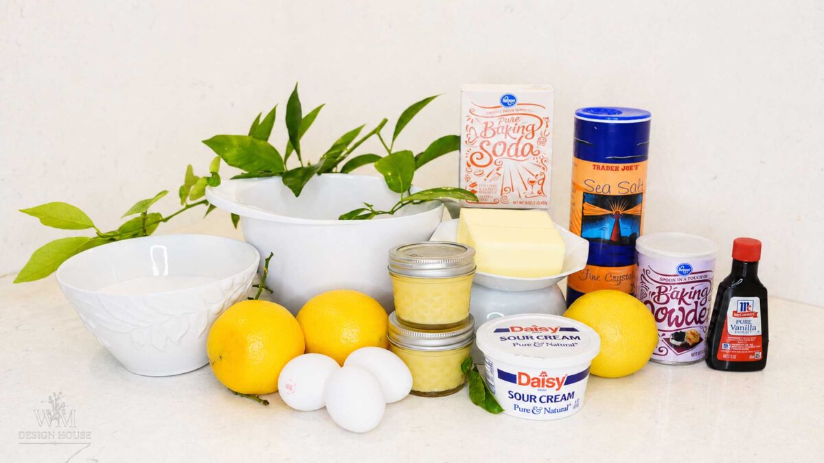 Ingredients for lemon bundt cake including fresh lemons, jars of lemon curd, sour cream, butter and eggs
