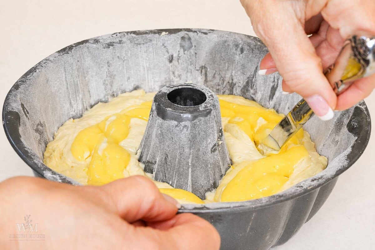 Hands spreading egg wash onto dough in a floured bundt pan with a brush, preparing it for baking.