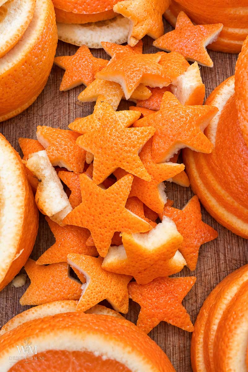 Several orange peels cut into star shapes are arranged on a wooden surface, surrounded by circular slices and sections of orange peel.