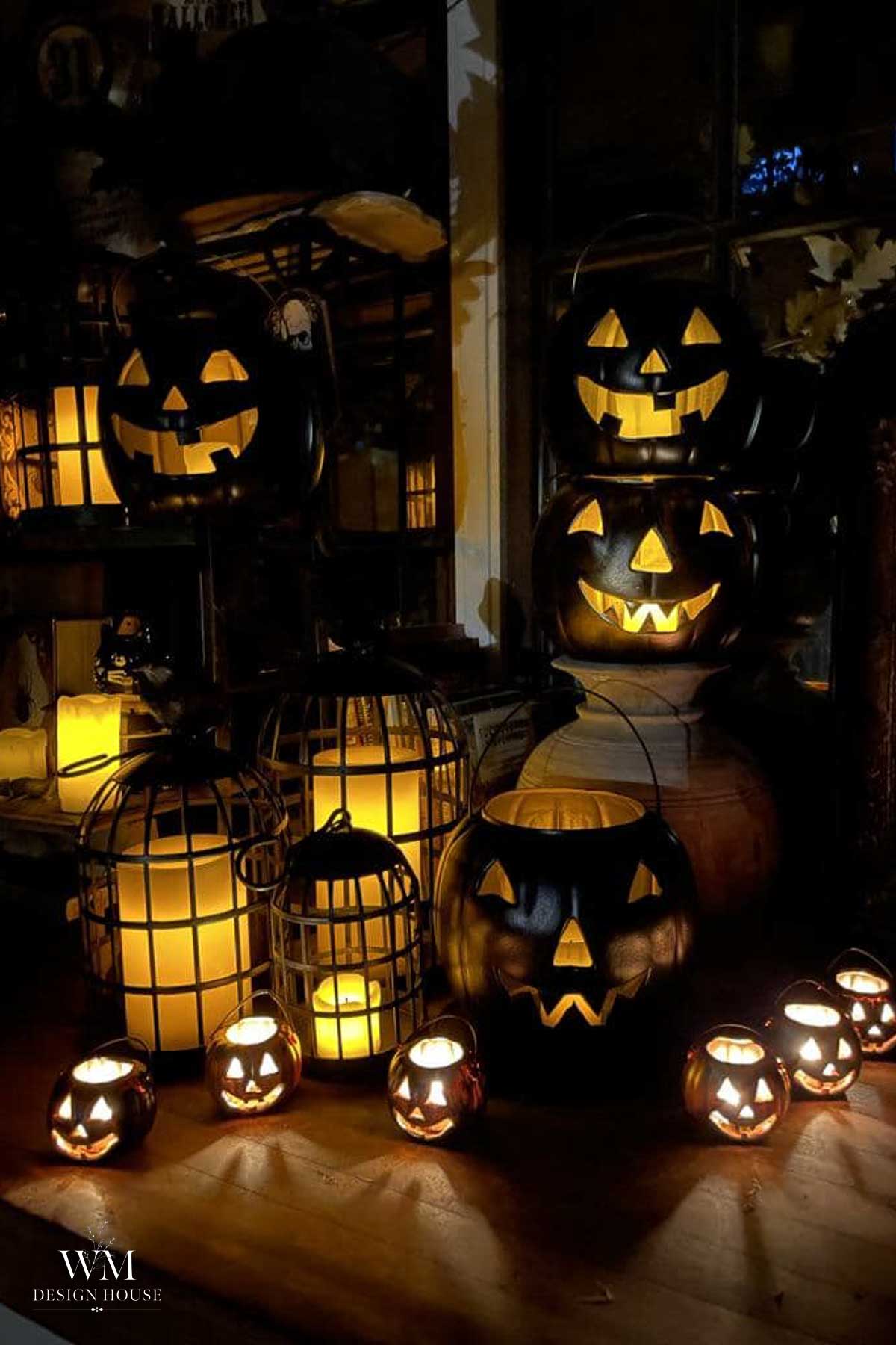 A group of glowing jack-o’-lanterns and candle lanterns of various sizes are arranged together in a dimly lit room, creating a spooky Halloween atmosphere.