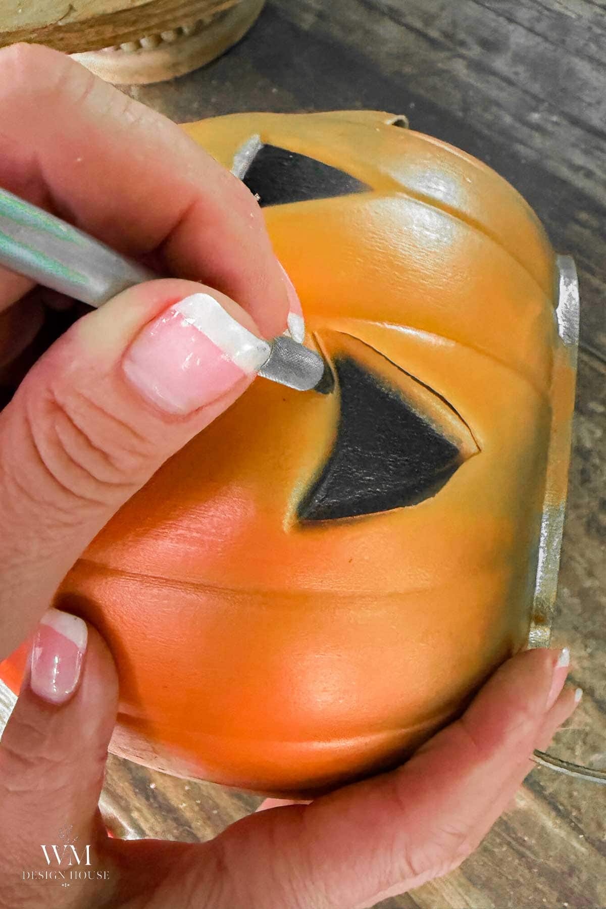 Craft knife cutting a triangle eye into a plastic pumpkin bucket for a Halloween lantern