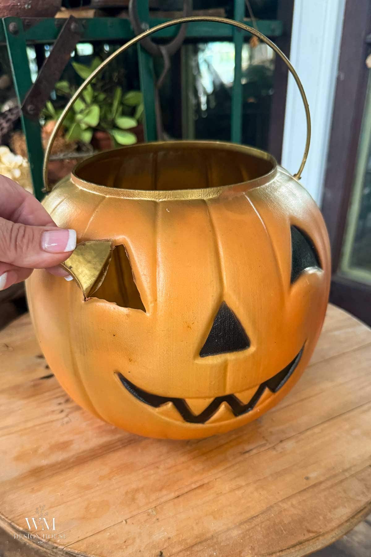 A hand pulls back  the eye of a plastic jack-o’-lantern candy bucket sitting on a wooden surface.
