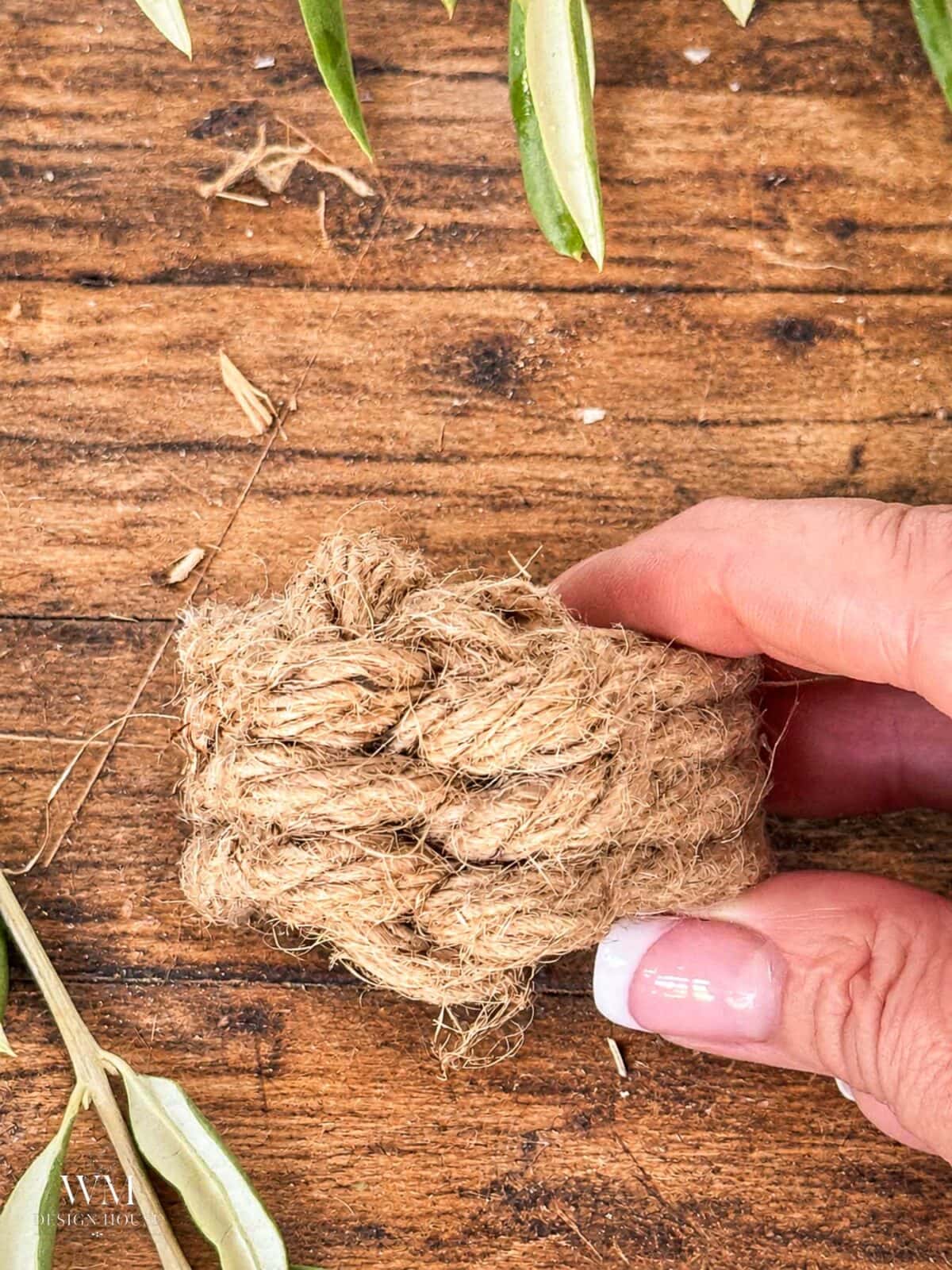 A hand holding a thick, circular jute rope napkin ring tied in a leaf knot. 