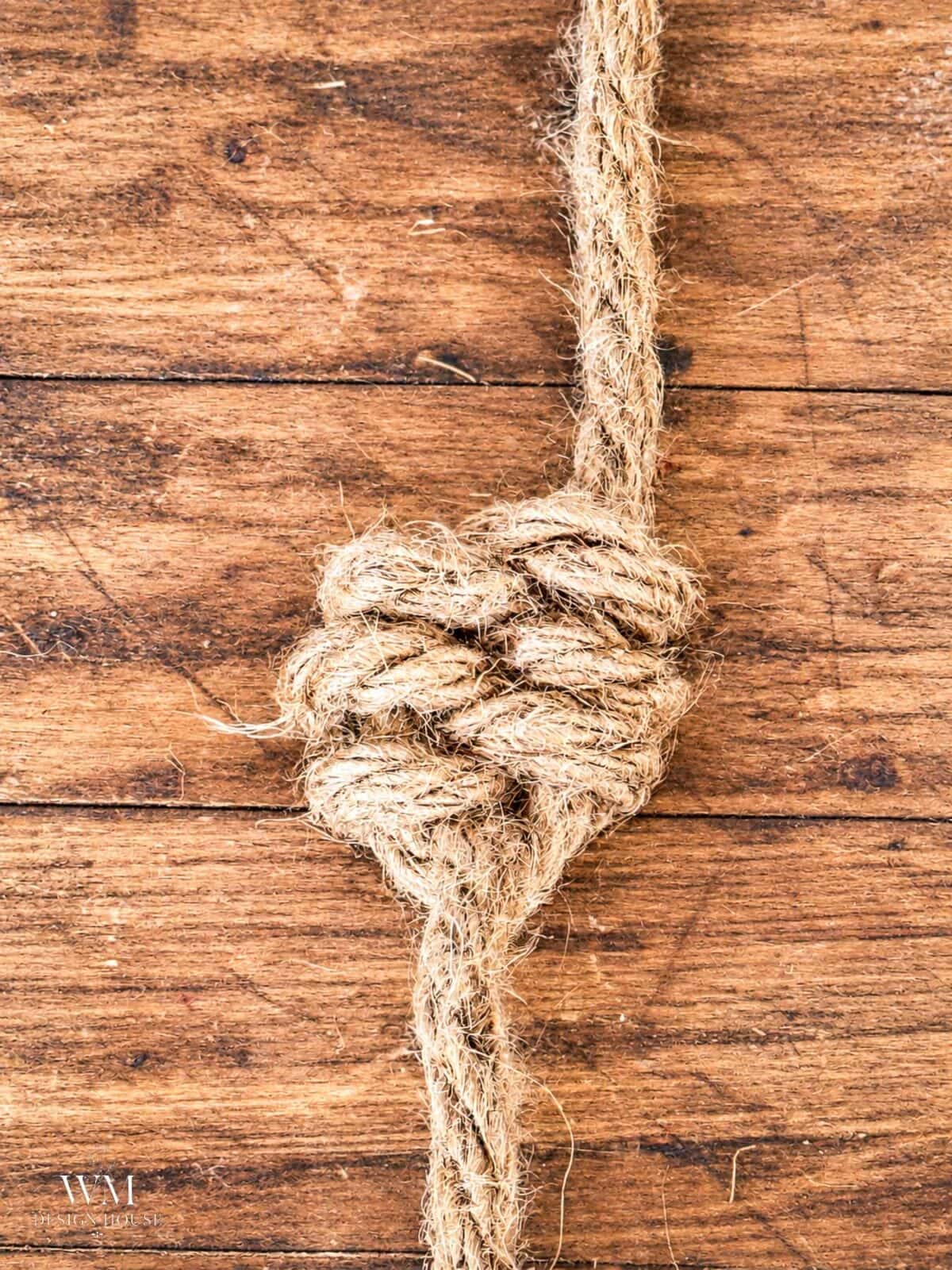 A thick, natural-fiber rope tied in a knot, resting on a wooden surface featuring the finished leaf knot. 