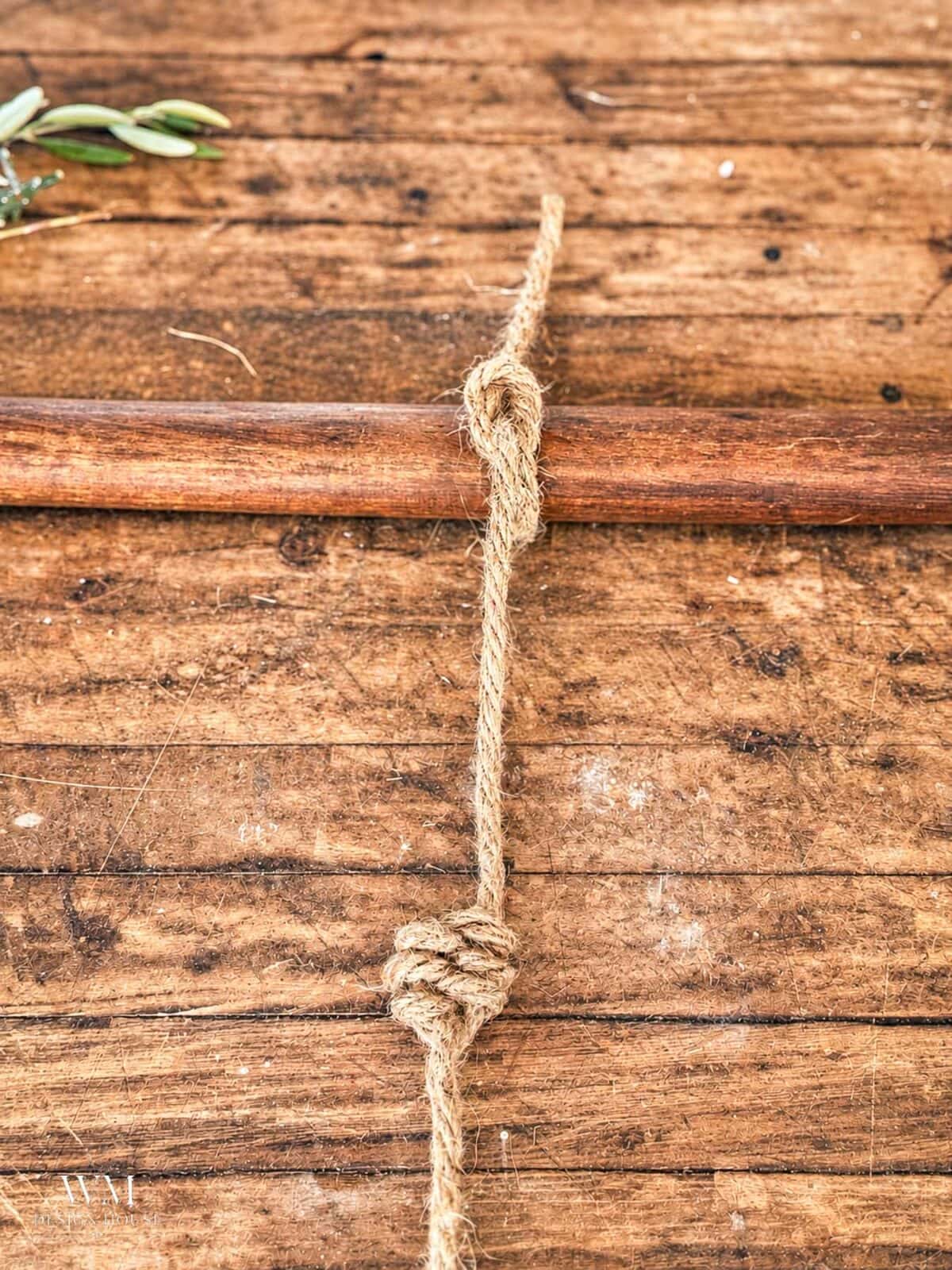 A length of jute rope tied around a wooden rod, featuring the finished leaf knot. 