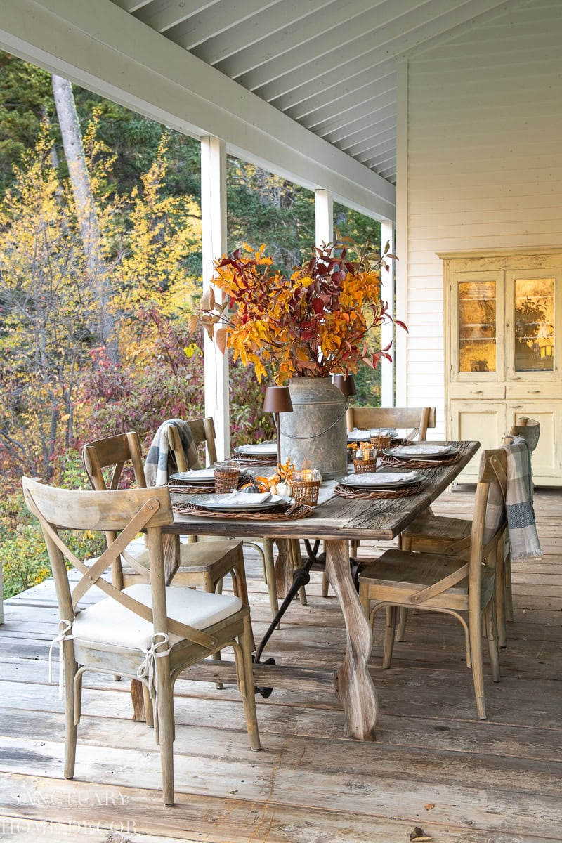 Rustic fall table on a covered porch with turning leaves in a galvanized bucket, from Sanctuary Home Decor.