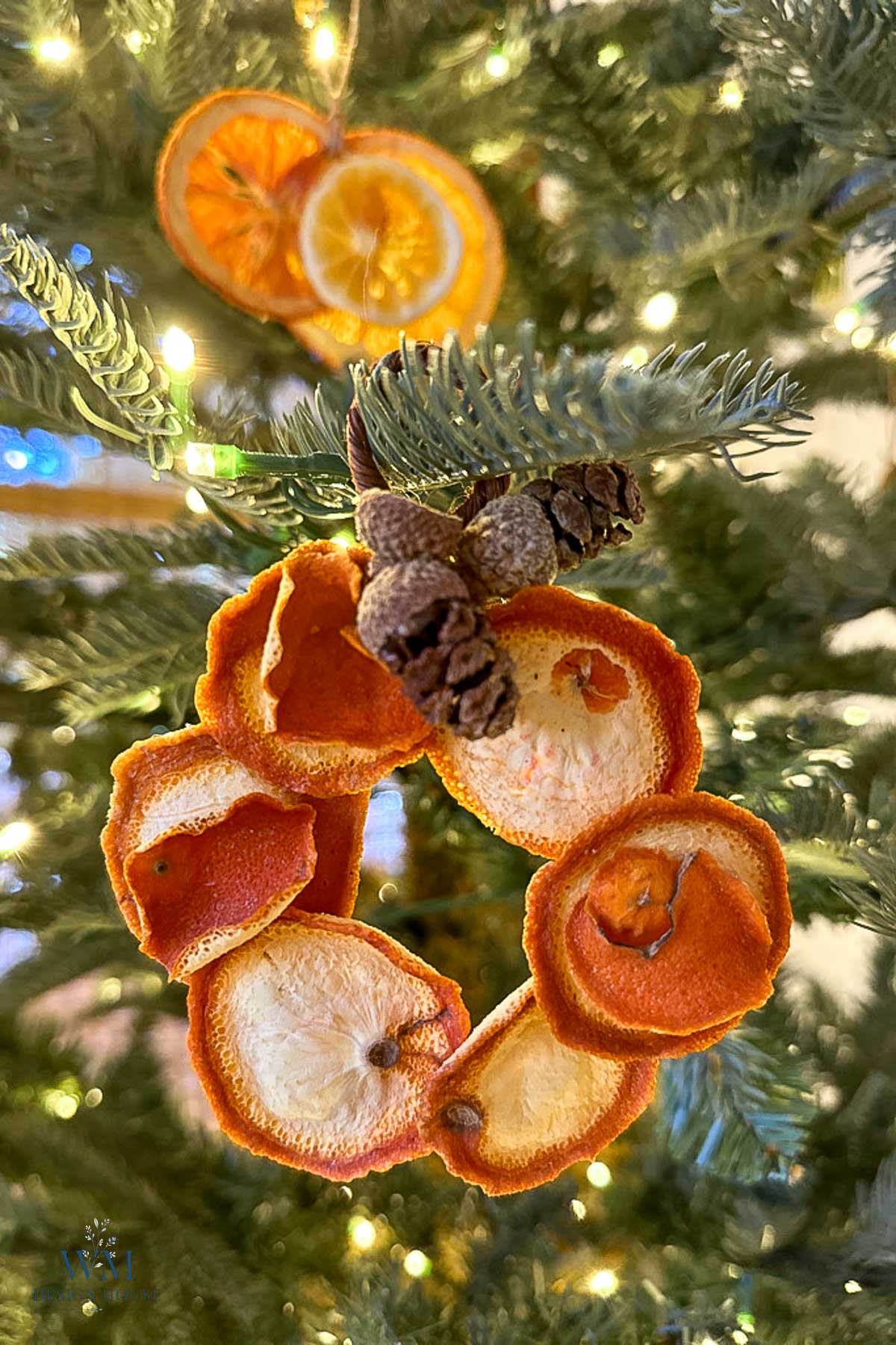 A wreath ornament made of dried orange slices and pinecones hanging on a lit Christmas tree.