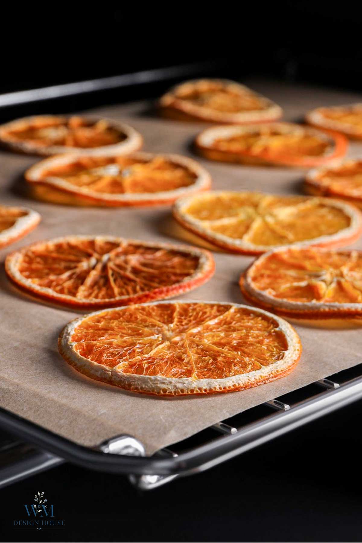 Several thin, dehydrated orange slices arranged on parchment paper on a baking sheet.
