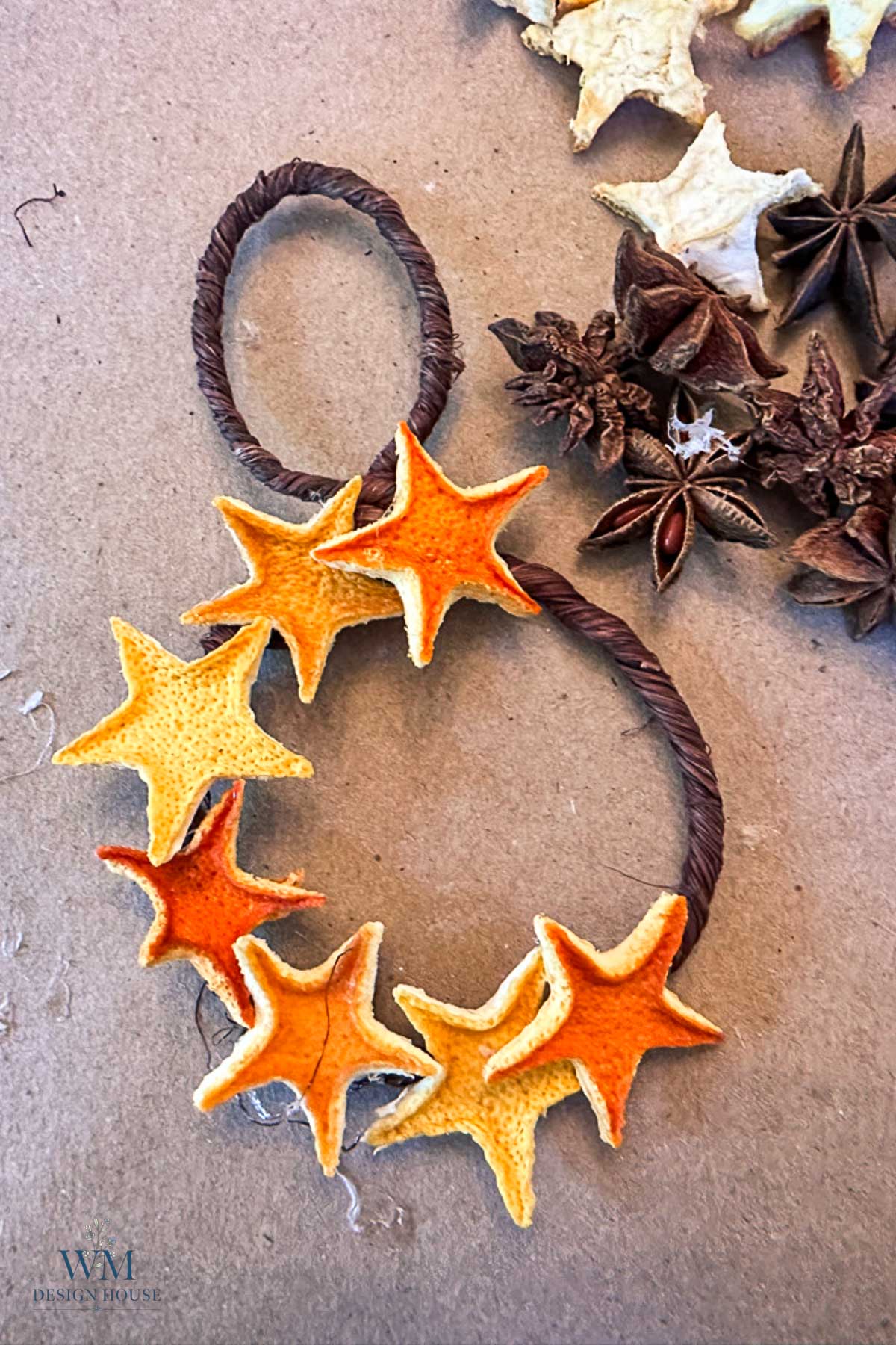 A wreath made from a dark twisted wire loop decorated with dried, star-shaped orange peel cutouts, surrounded by whole star anise.