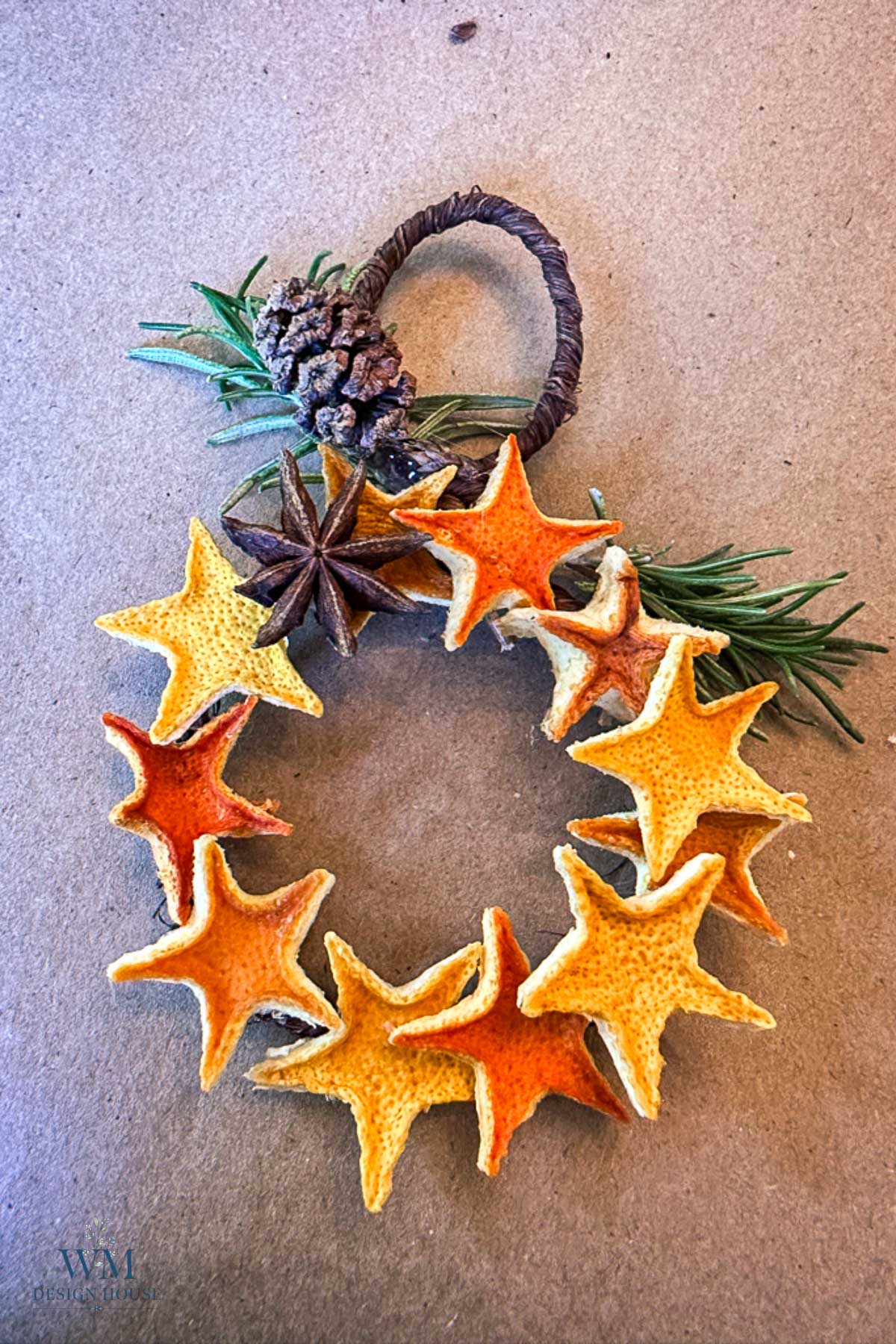 A small wreath made of star-shaped dried orange peels, garnished with a pinecone, star anise, and rosemary sprigs.