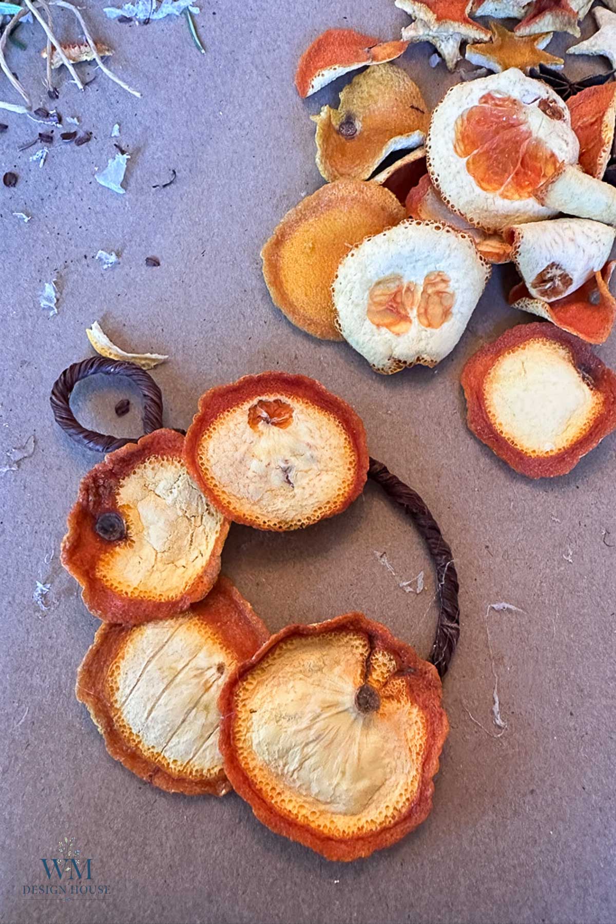 Dried orange slices and two small wreaths made of twisted vine on a brown surface.